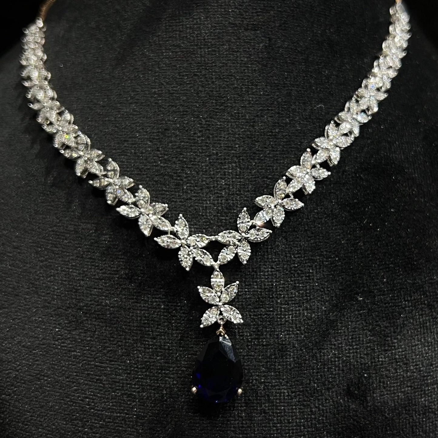 Close-up of diamond necklace set showing detailed floral design and pear-shaped color stone drop pendant on a mannequin bust.
