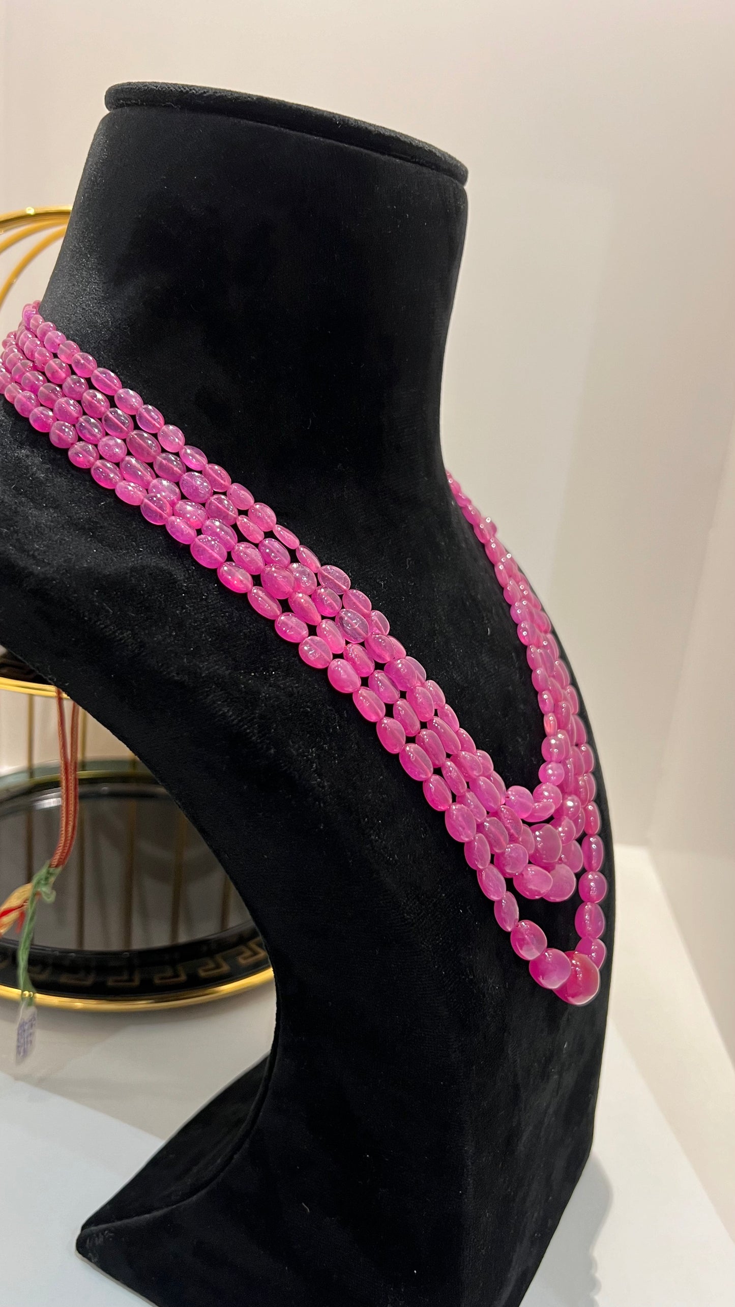 A black mannequin necklace displaying a multi-layered pink ruby beaded necklace with adjustable Dori.