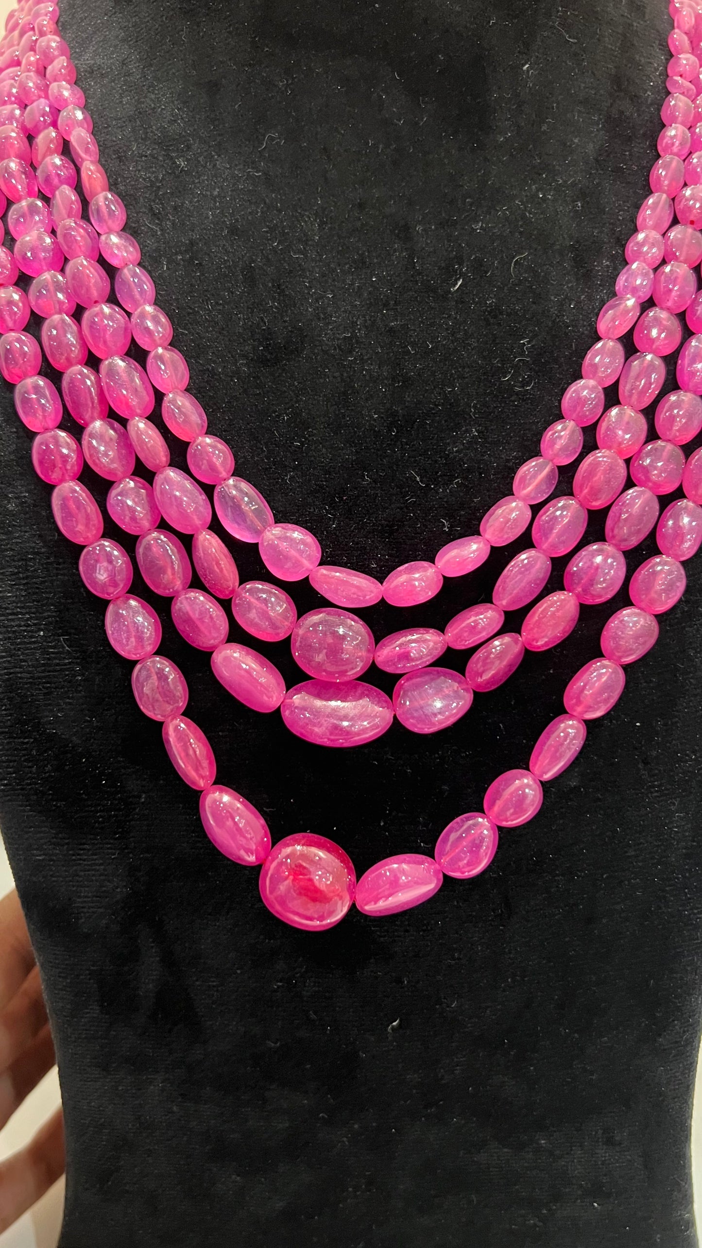 A black mannequin necklace displaying a multi-layered pink ruby beaded necklace with adjustable Dori.