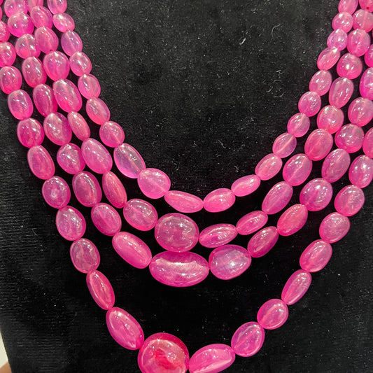 A black mannequin necklace displaying a multi-layered pink ruby beaded necklace with adjustable Dori.