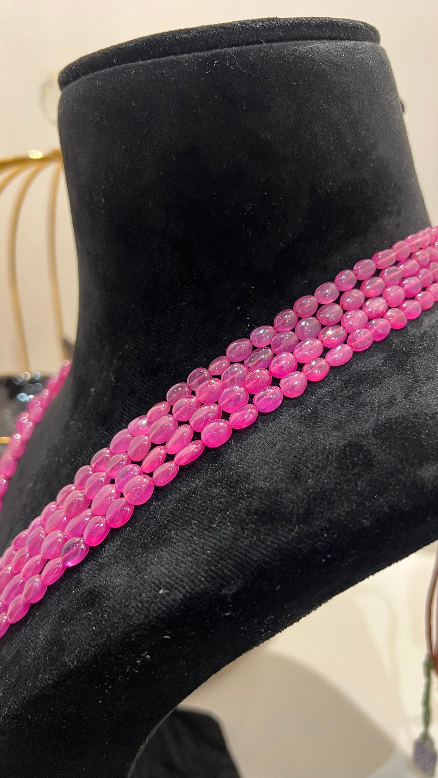 A black mannequin necklace displaying a multi-layered pink ruby beaded necklace with adjustable Dori.