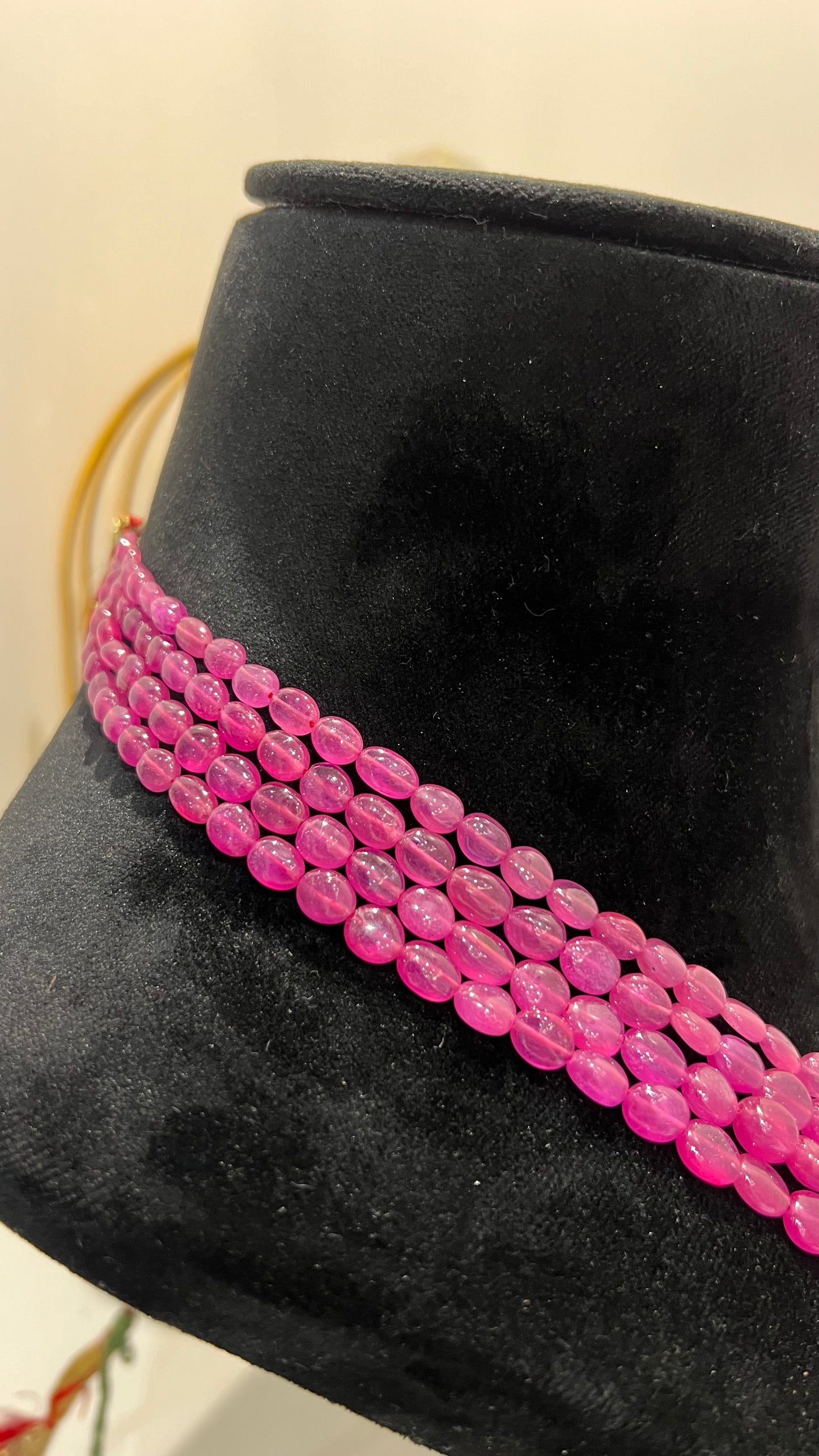 A black mannequin necklace displaying a multi-layered pink ruby beaded necklace with adjustable Dori.