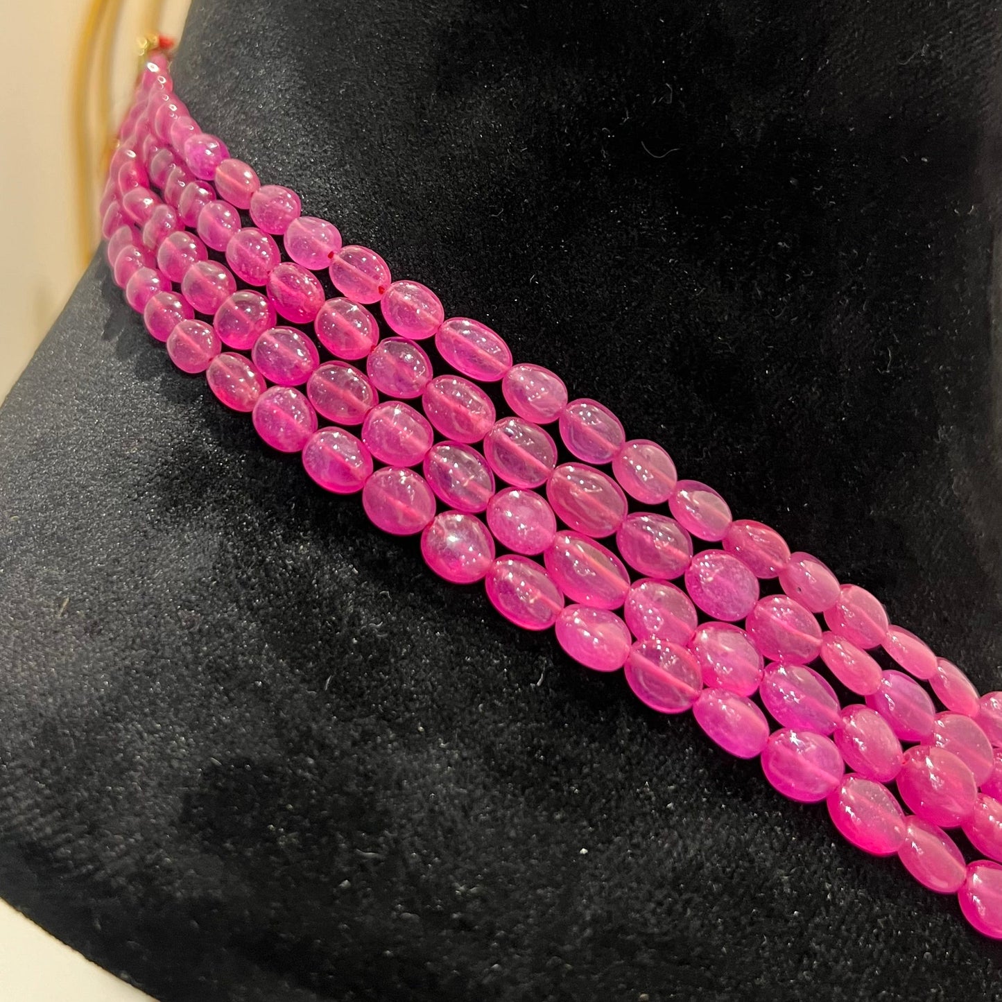 A black mannequin displaying a multi-layered pink ruby beaded necklace with adjustable Dori.