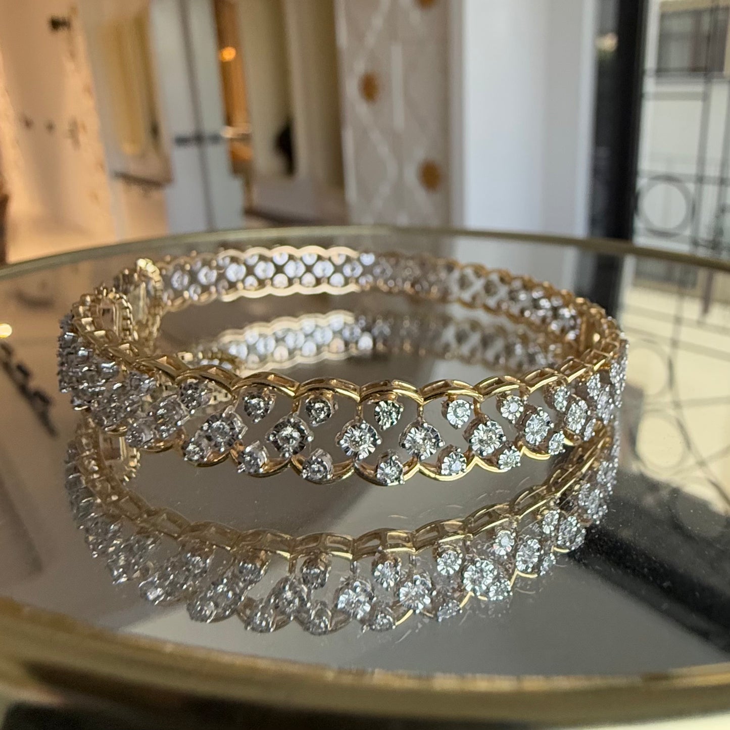 A luxurious diamond gold tennis bracelet with openable sections, featuring gold color and adorned with genuine diamonds, displayed on a glass.