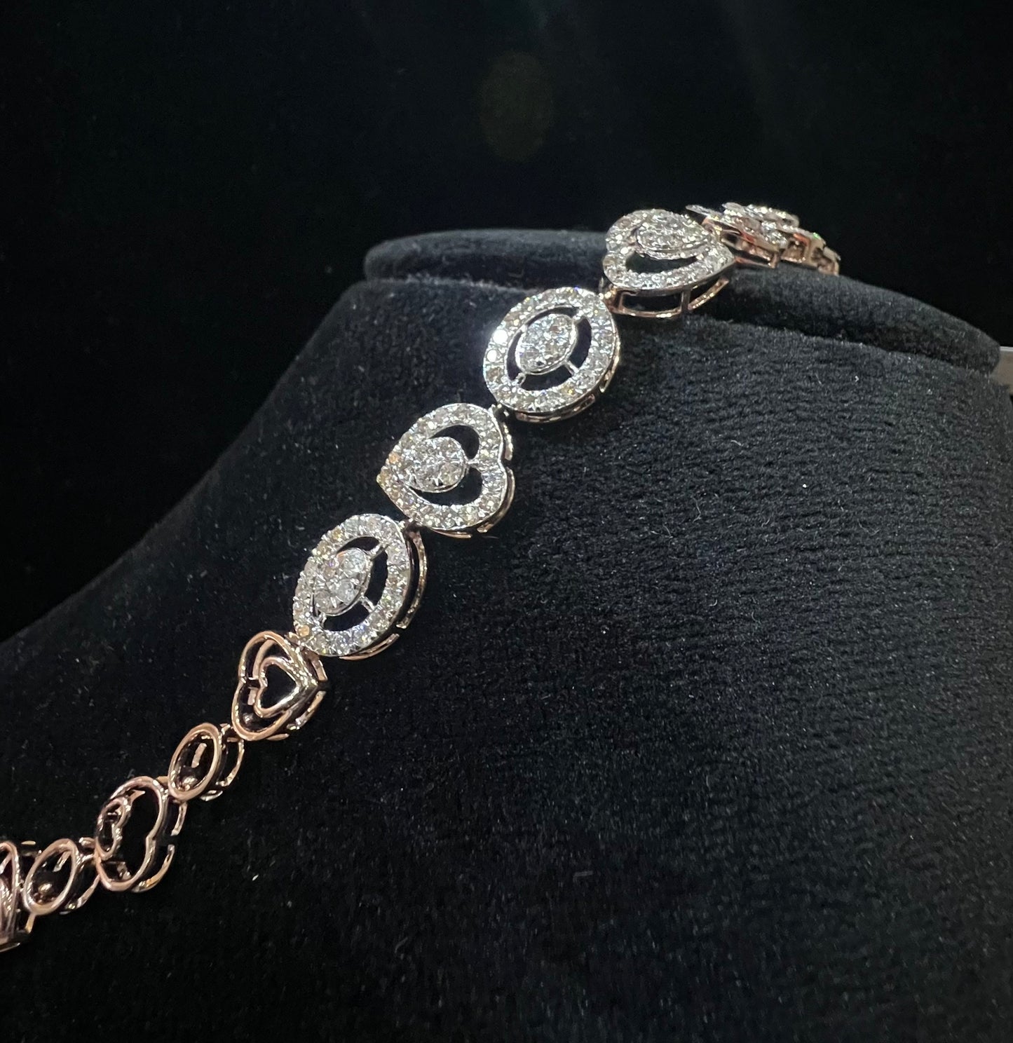 A gold diamond bracelet with oval heart shapes, displayed on a black mannequin.