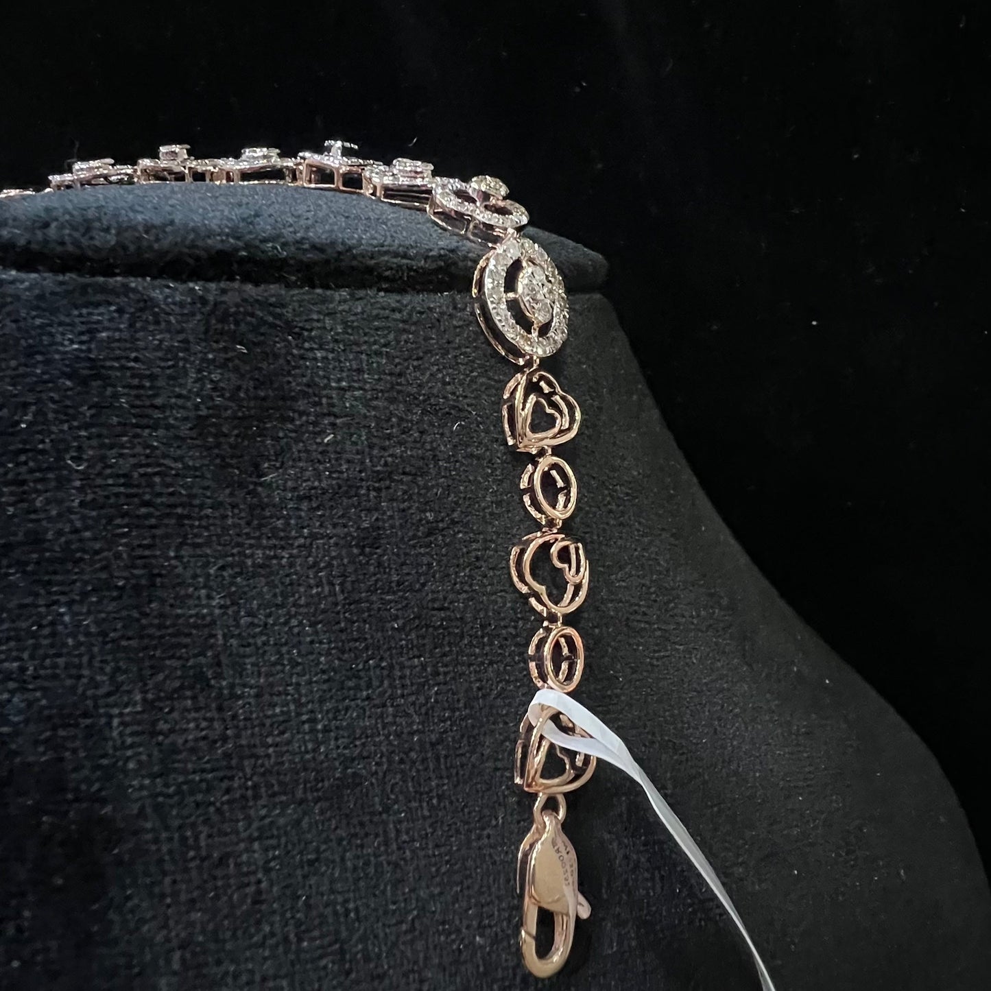 A gold diamond bracelet with oval heart shapes, displayed on a black mannequin.