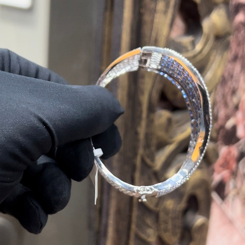 A close-up image of a hand holding a luxurious gold diamond bracelet with a sparkling blue stone, showing an openable design.