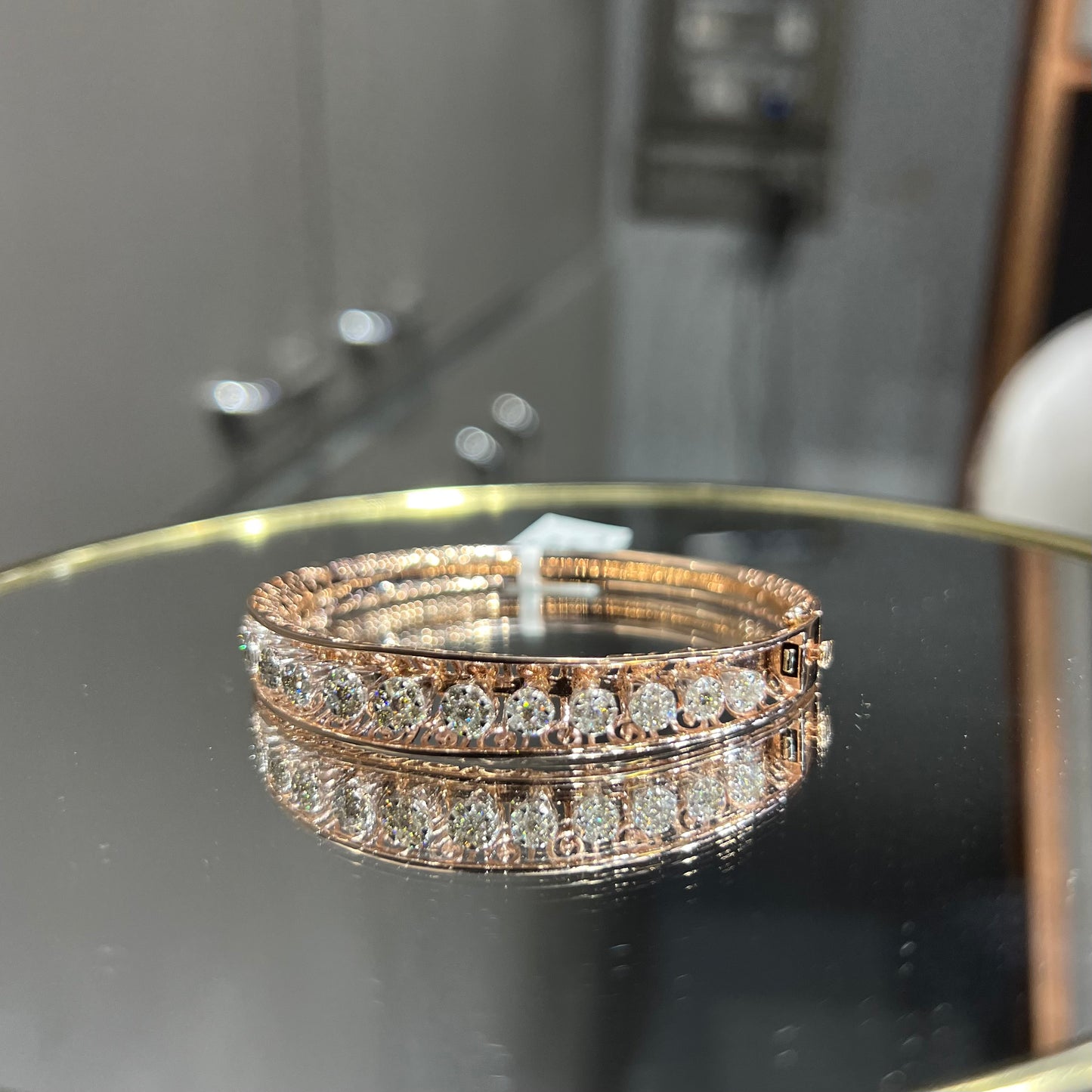 Elegant gold diamond bracelet with round-cut diamonds in a bangle design, displayed on a reflective surface.