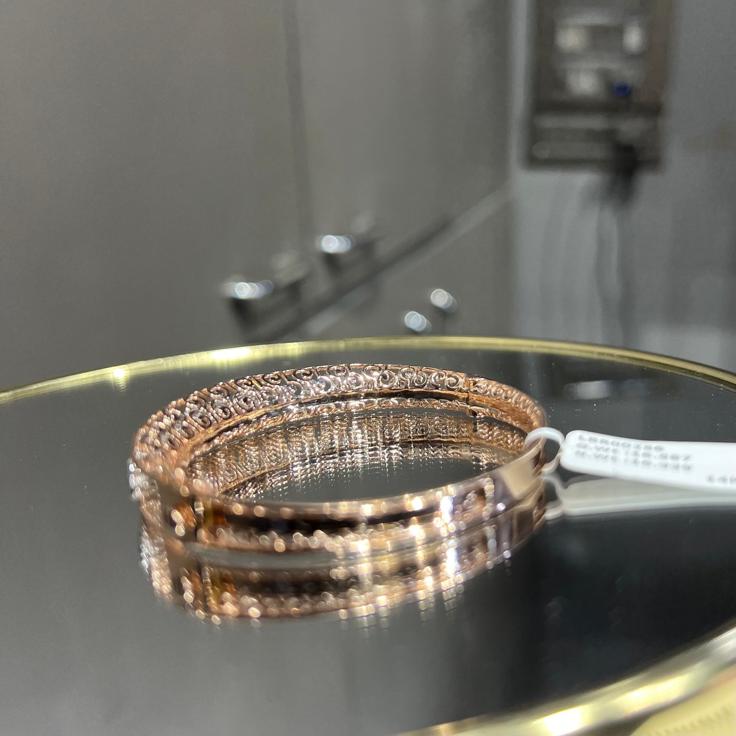 Elegant gold diamond bracelet with round-cut diamonds in a bangle design, displayed on a reflective surface.