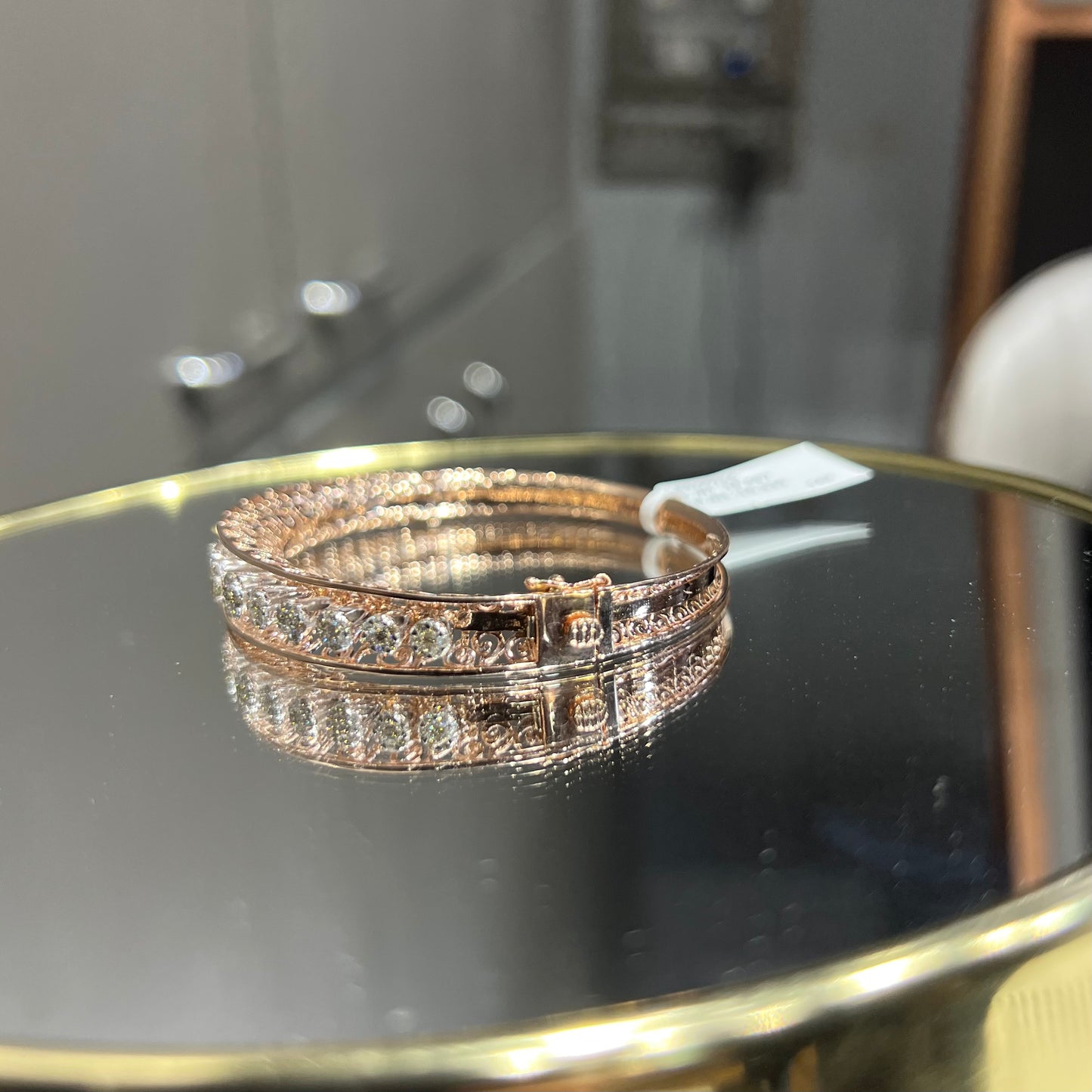 Elegant gold diamond bracelet with round-cut diamonds in a bangle design, displayed on a reflective surface.