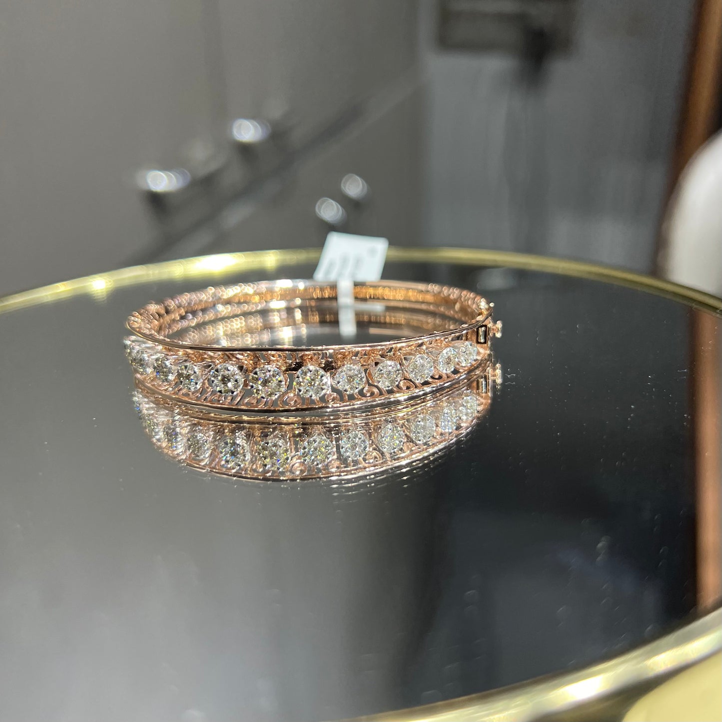 Elegant gold diamond bracelet with round-cut diamonds in a bangle design, displayed on a reflective surface.