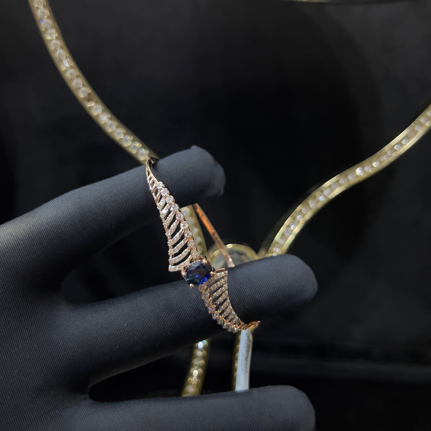 A luxurious gold diamond bracelet with a brilliant cut blue stone in an openable design, displayed by a hand.