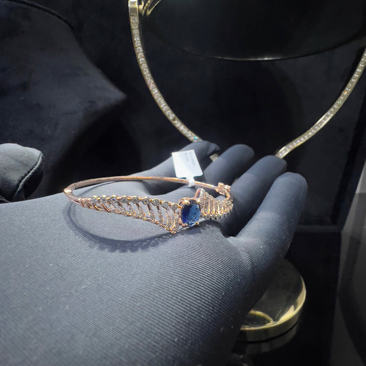 A luxurious gold diamond bracelet with a brilliant cut blue stone in an openable design, displayed on a hand.