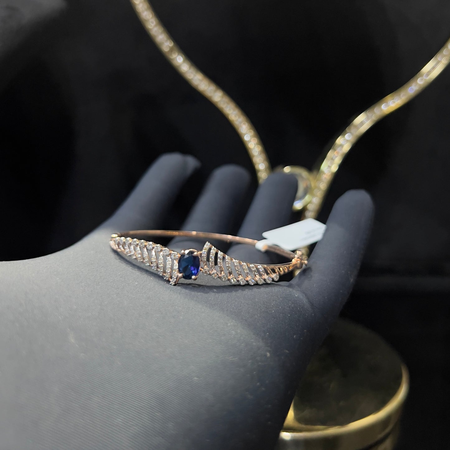 A luxurious gold diamond bracelet with a brilliant cut blue stone in an openable design, displayed on a hand.