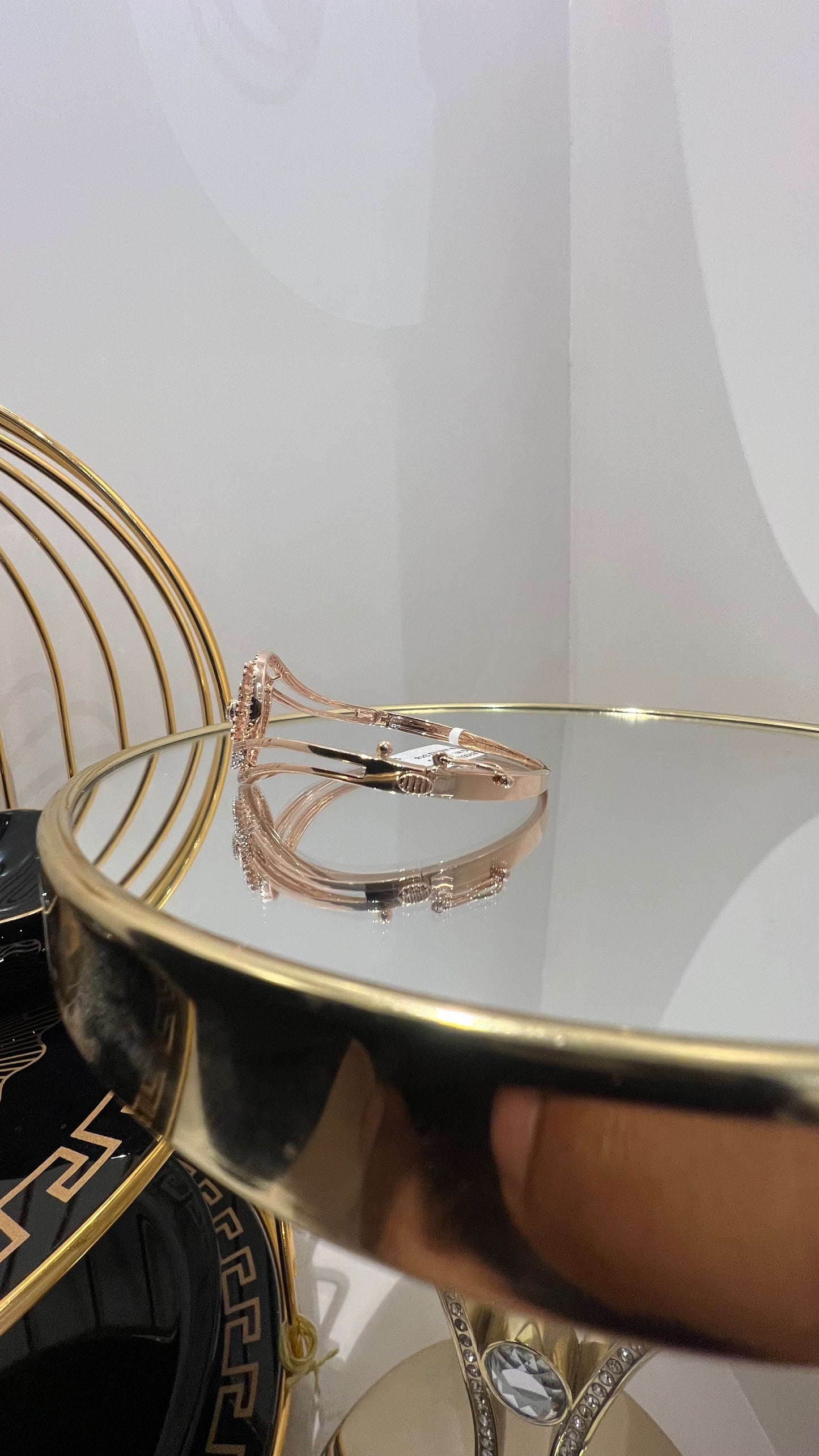 A luxurious gold diamond bracelet with a openable design, featuring a central oval-shaped diamond surrounded by smaller diamonds set in a brilliant cut, displayed on a reflective surface.