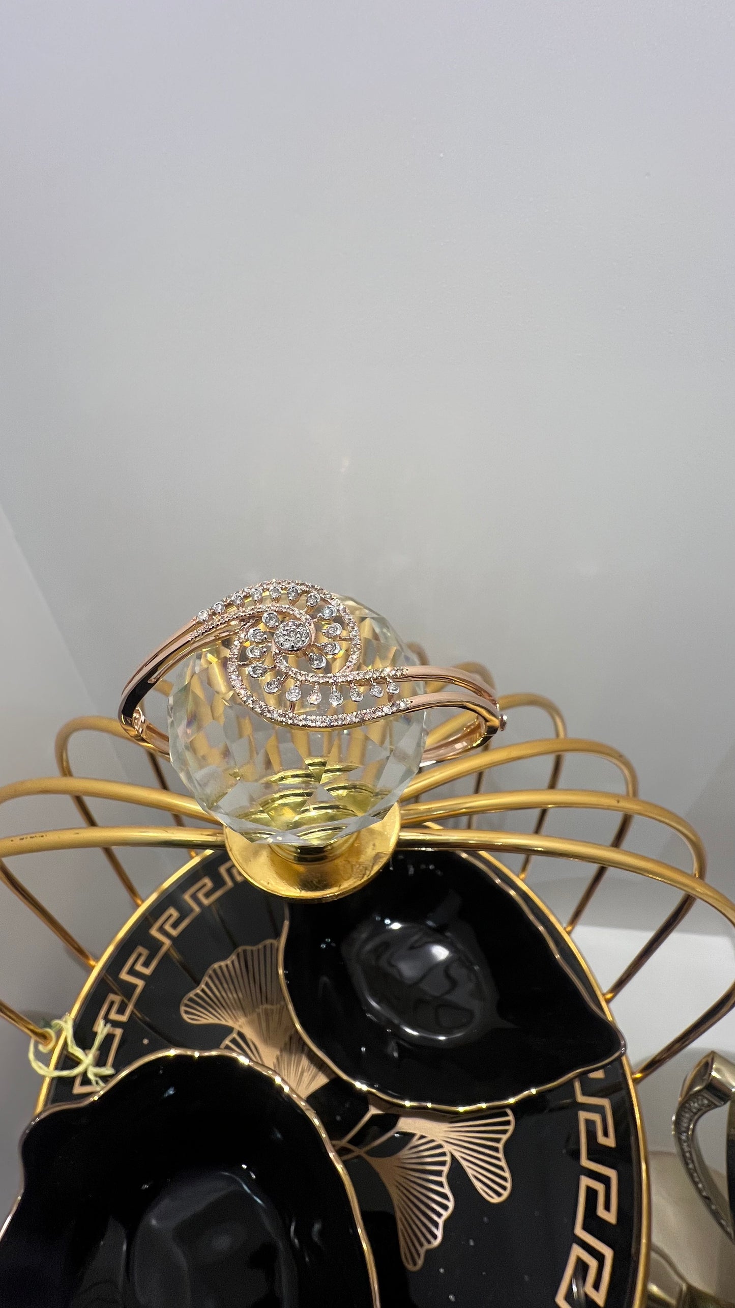 A luxurious gold diamond bracelet with a openable design, featuring a central oval-shaped diamond surrounded by smaller diamonds set in a brilliant cut, displayed on a glass ball.