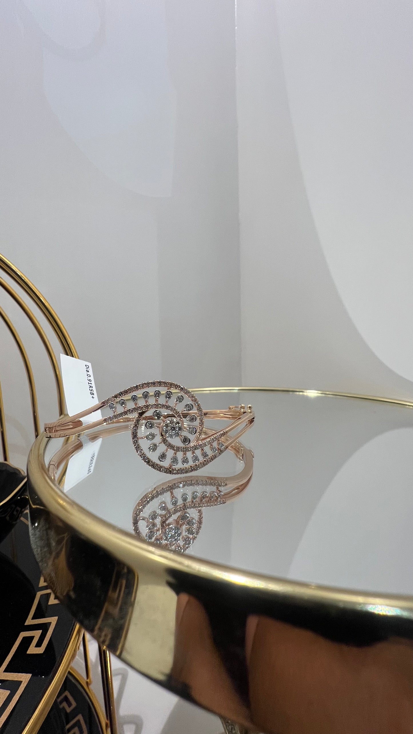 A luxurious gold diamond bracelet with a openable design, featuring a central oval-shaped diamond surrounded by smaller diamonds set in a brilliant cut, displayed on a reflective surface.