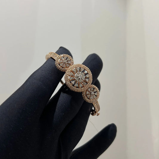 A gold diamond bracelet with a central oval-shaped diamond surrounded by smaller diamonds, displayed by a hand.