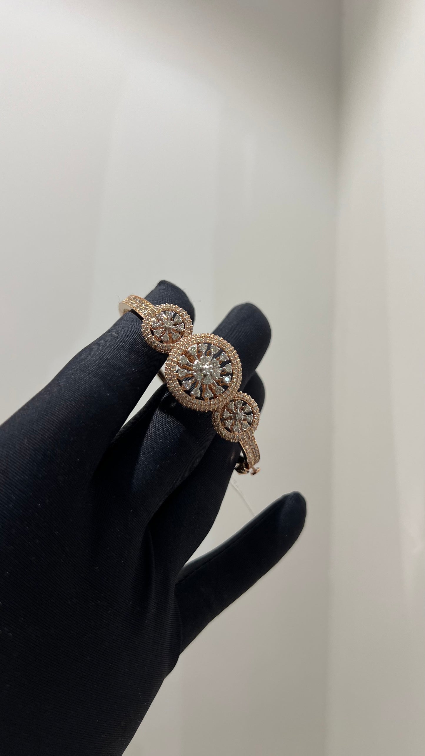 A gold diamond bracelet with a central oval-shaped diamond surrounded by smaller diamonds, displayed by a hand.
