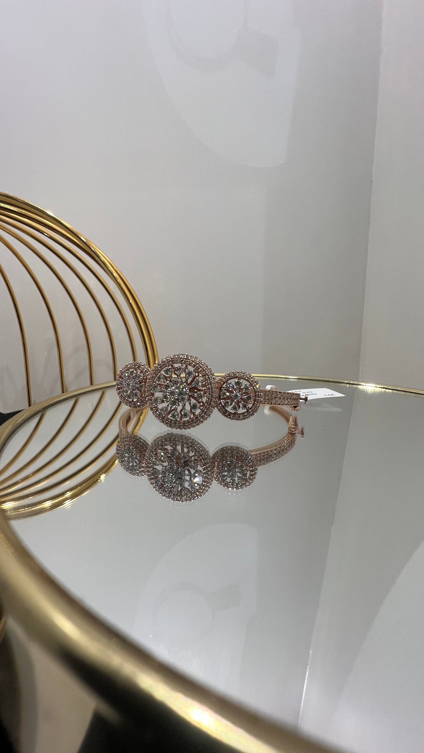 A gold diamond bracelet with a central oval-shaped diamond surrounded by smaller diamonds, displayed on a reflective surface.