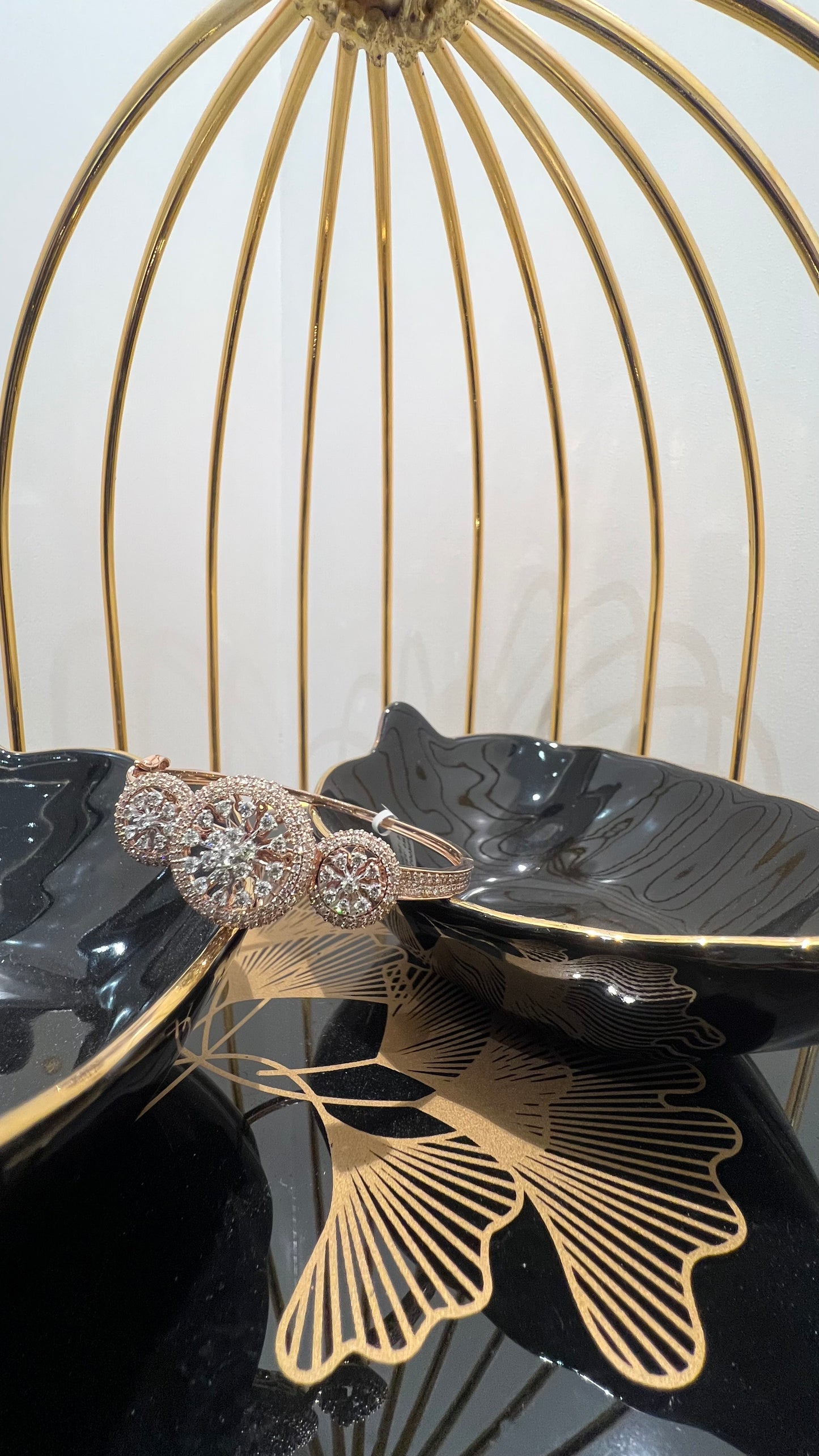 A gold diamond bracelet with a central oval-shaped diamond surrounded by smaller diamonds, displayed on a black surface.