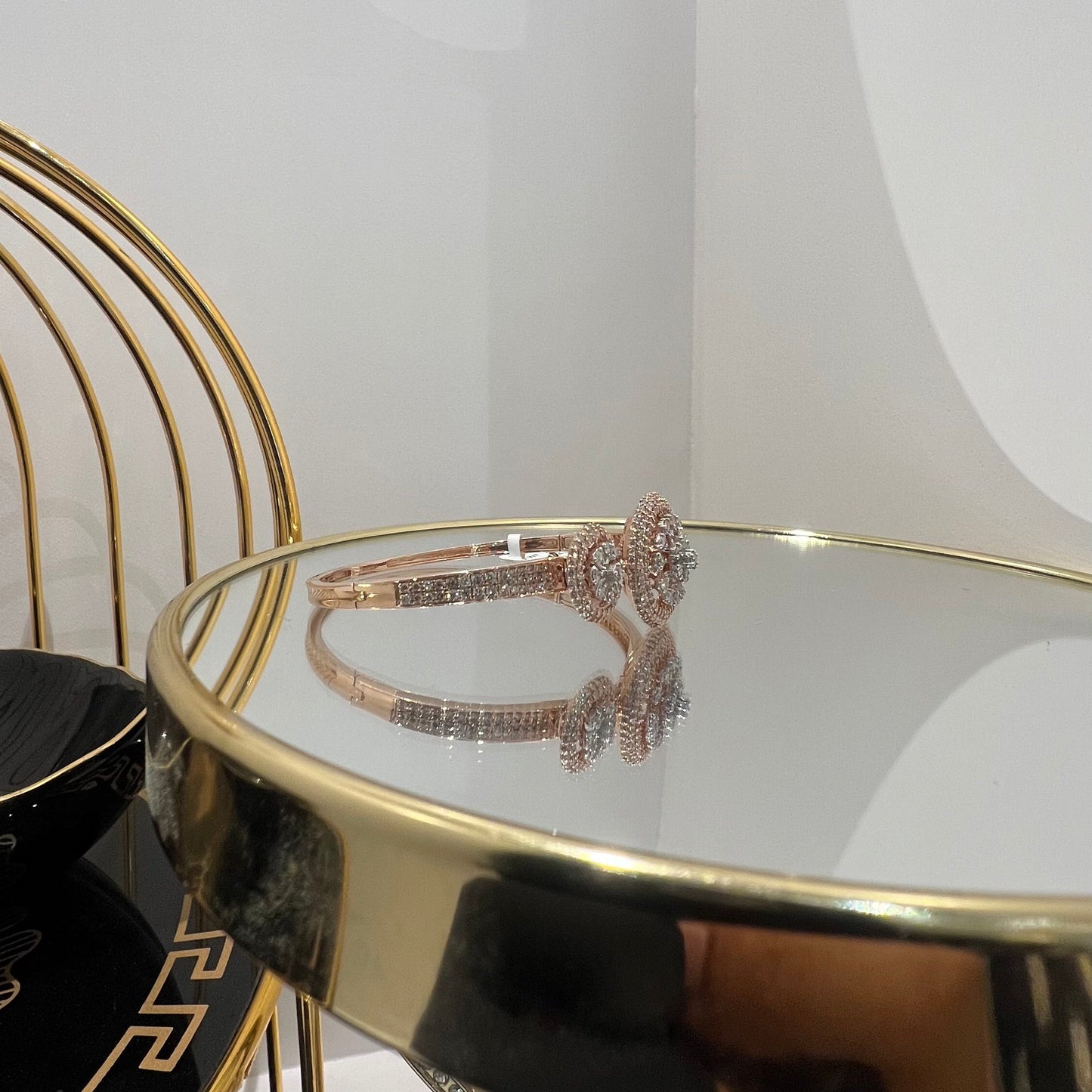 A gold diamond bracelet with a central oval-shaped diamond surrounded by smaller diamonds, displayed on a reflective surface.