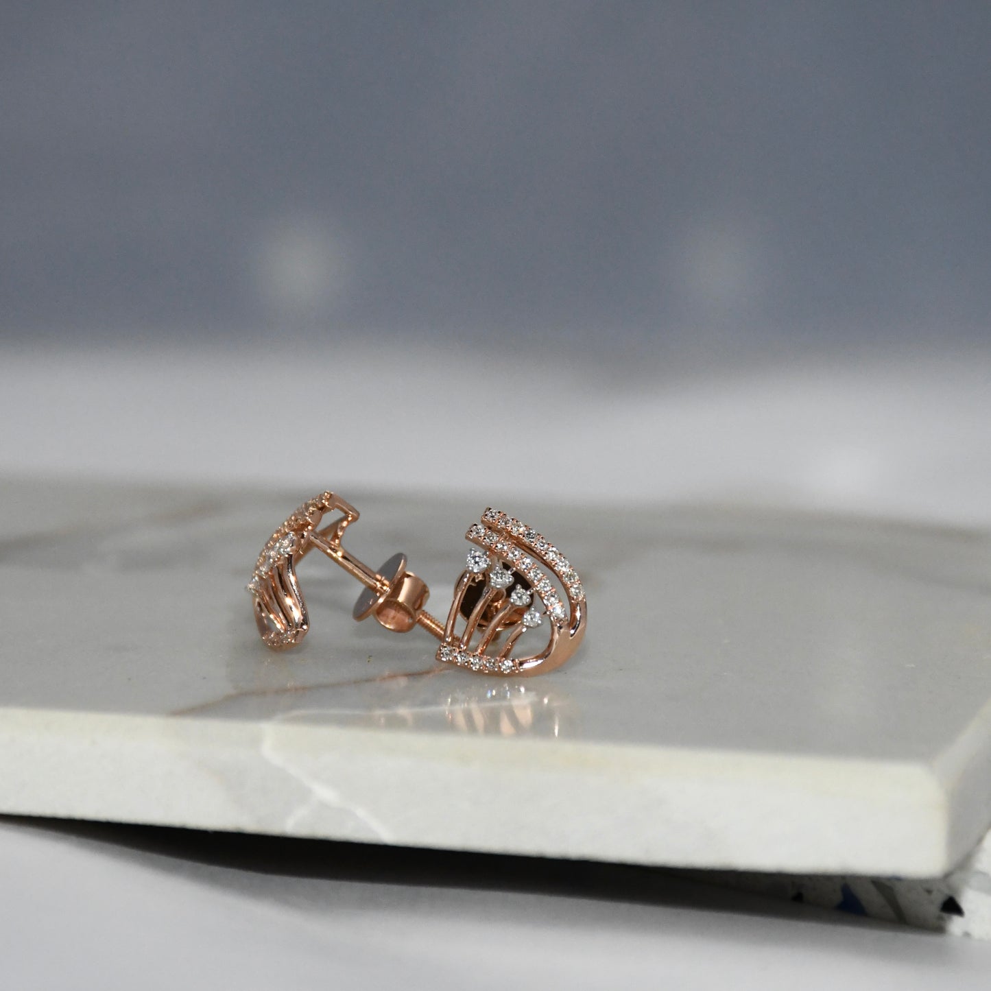 Rose gold earrings with diamonds on a marble surface