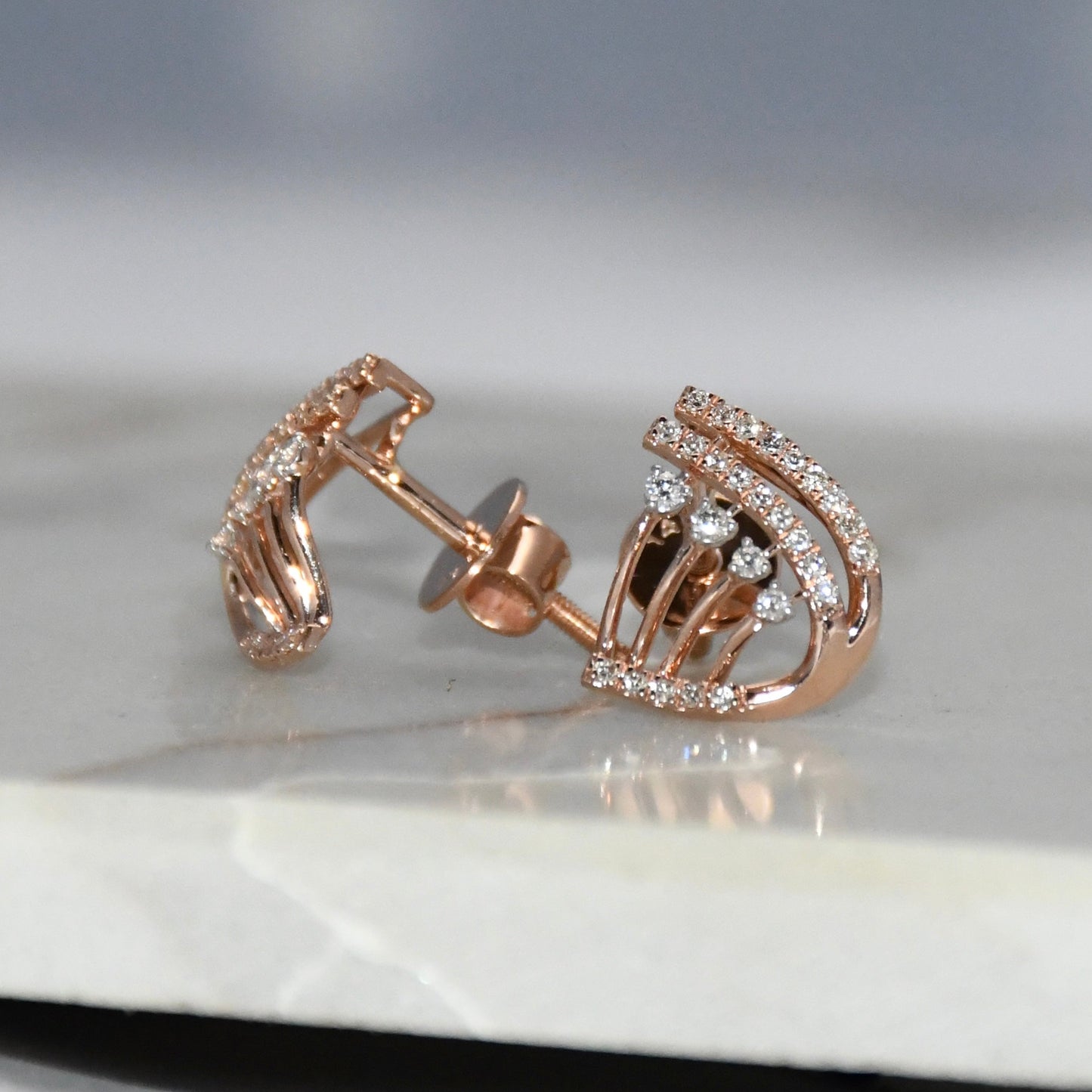 Rose gold earrings with diamond accents on a reflective surface