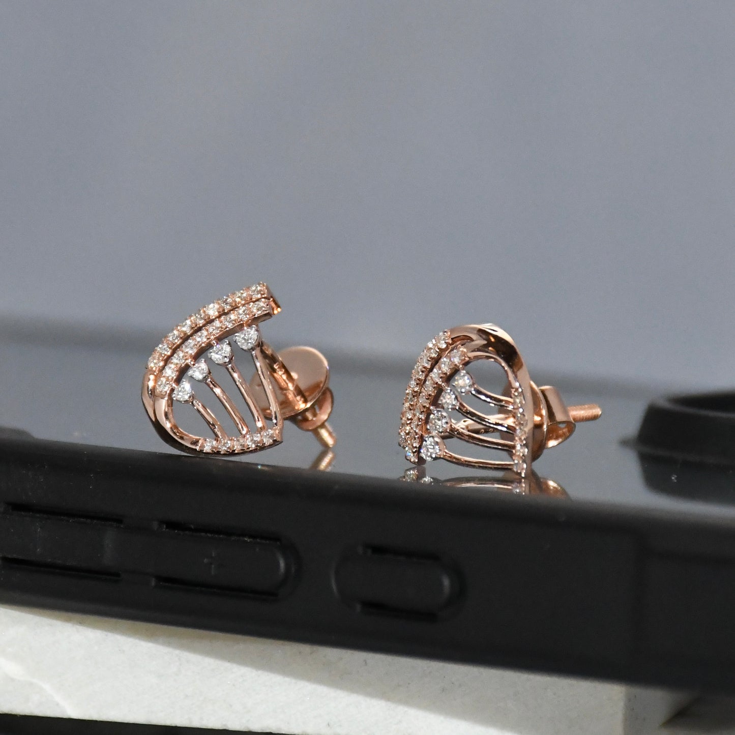 Rose gold earrings with diamonds on a reflective surface