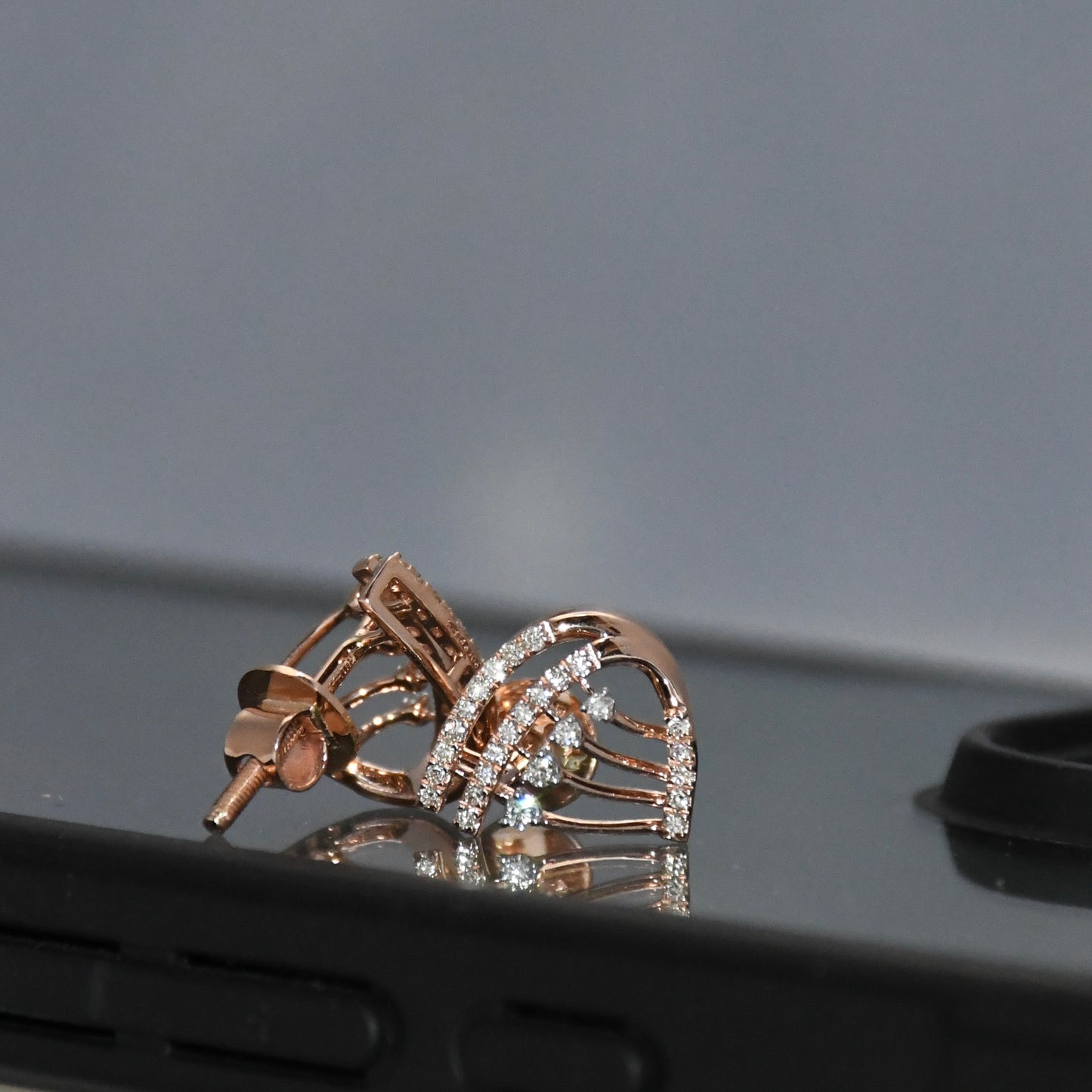Rose gold earrings with diamonds on a reflective surface