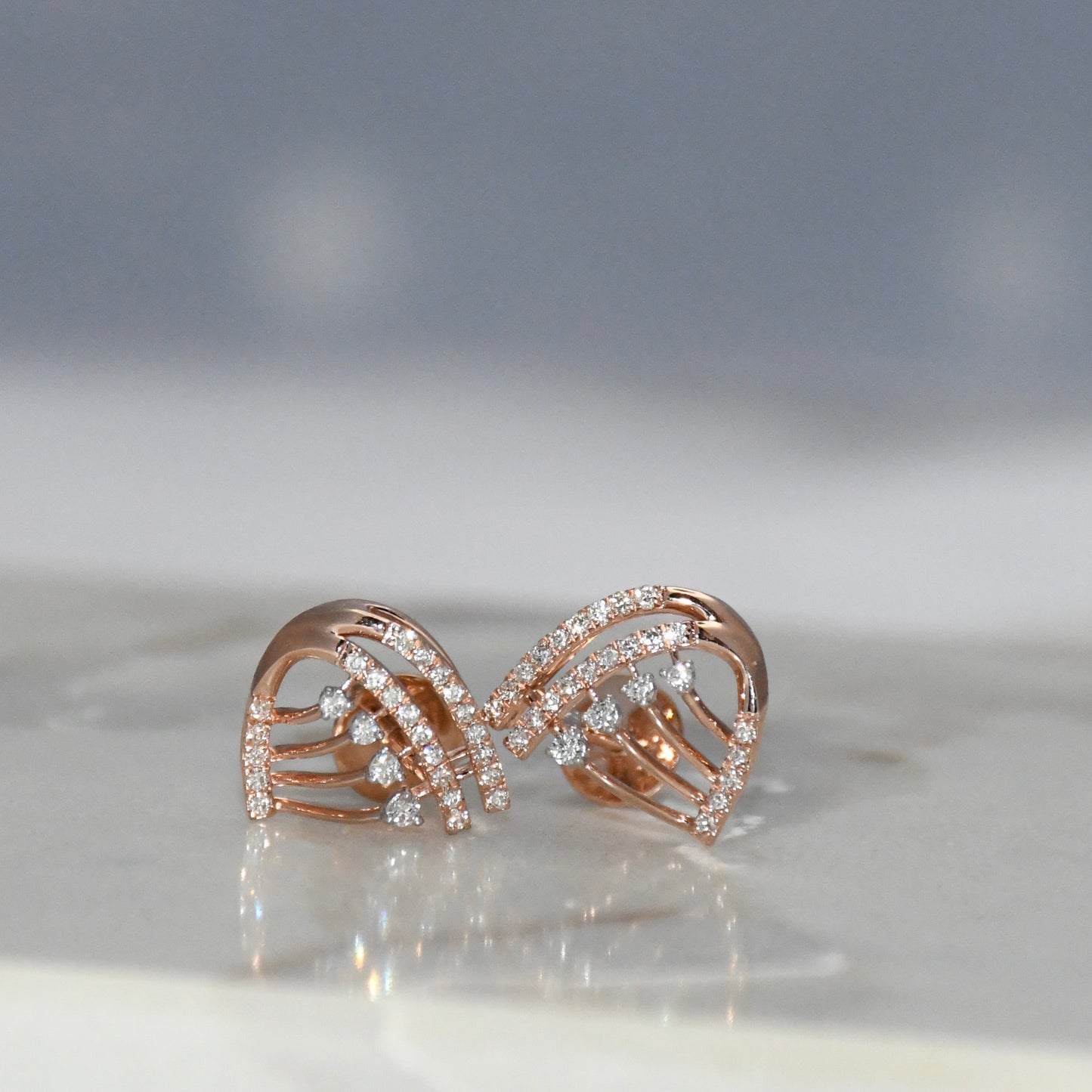 Rose gold butterfly-shaped earrings with clear diamonds on a reflective surface.