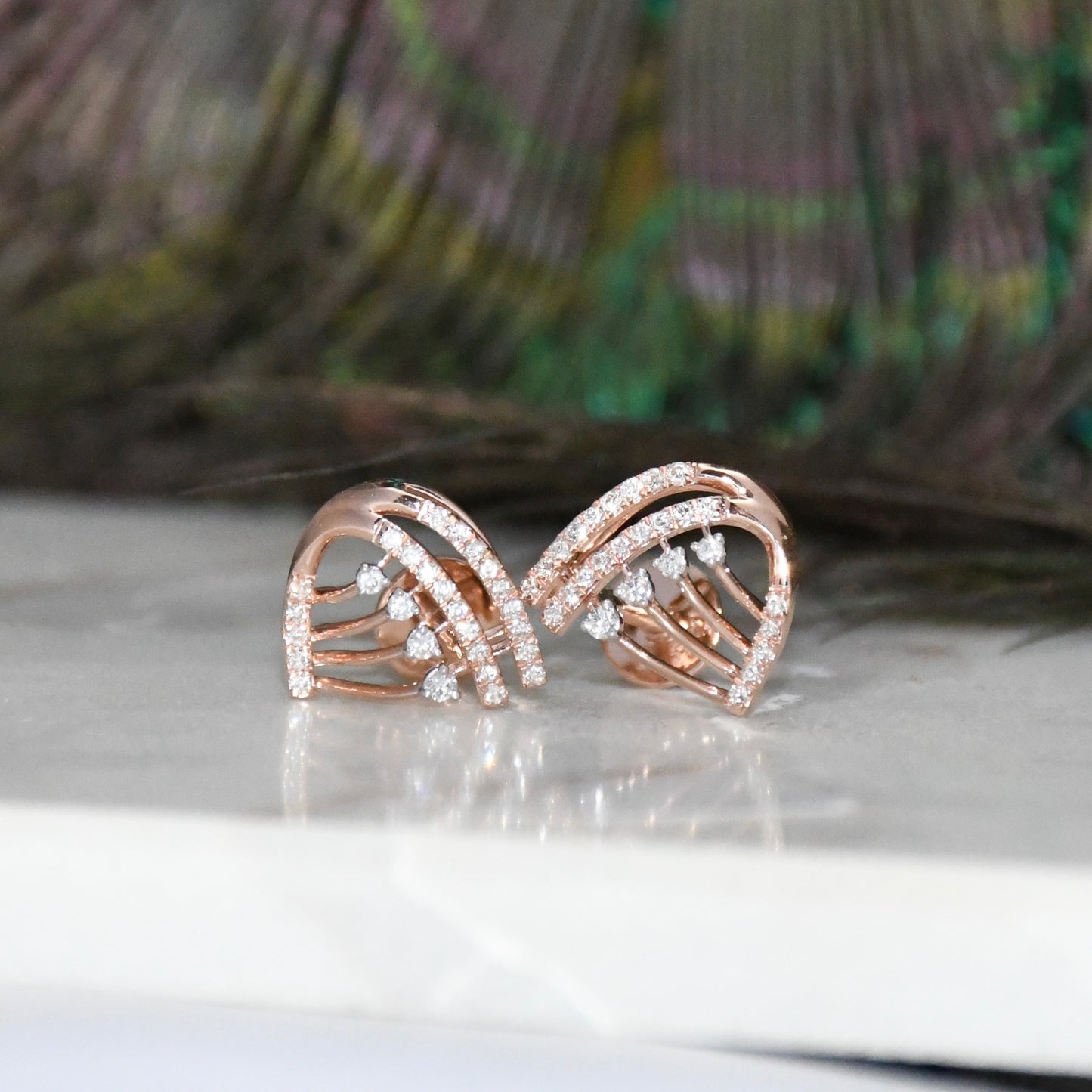 Rose gold earrings with diamond accents on a reflective surface