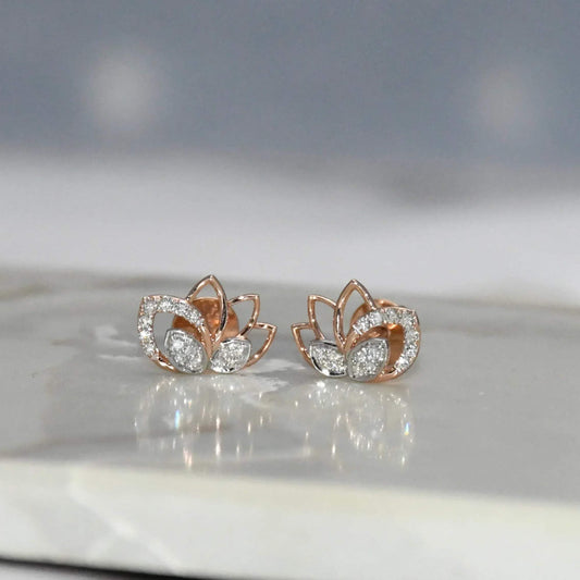 Rose gold lotus flower earrings with clear diamonds on a reflective surface.