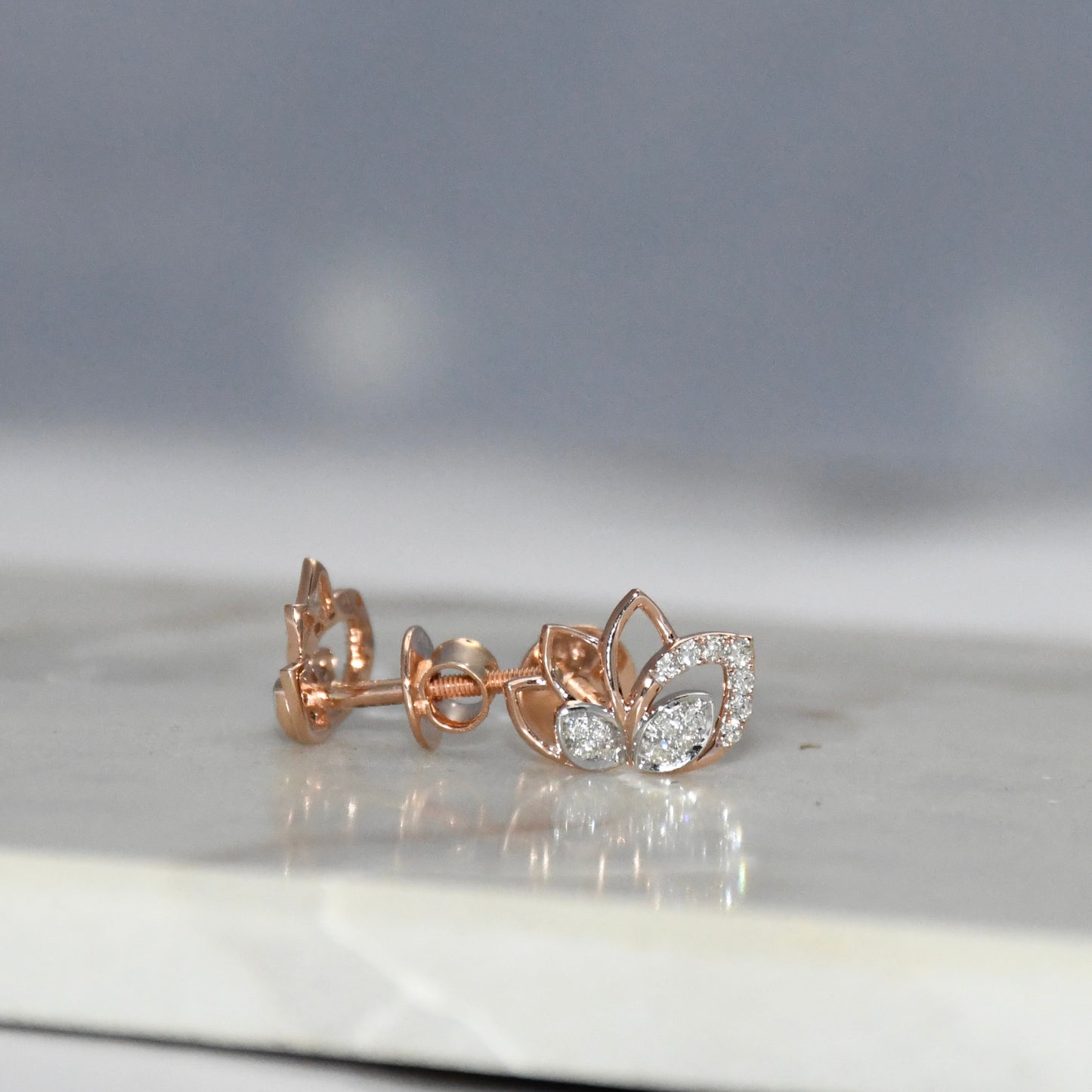 Rose gold earrings with diamond accents on a reflective surface