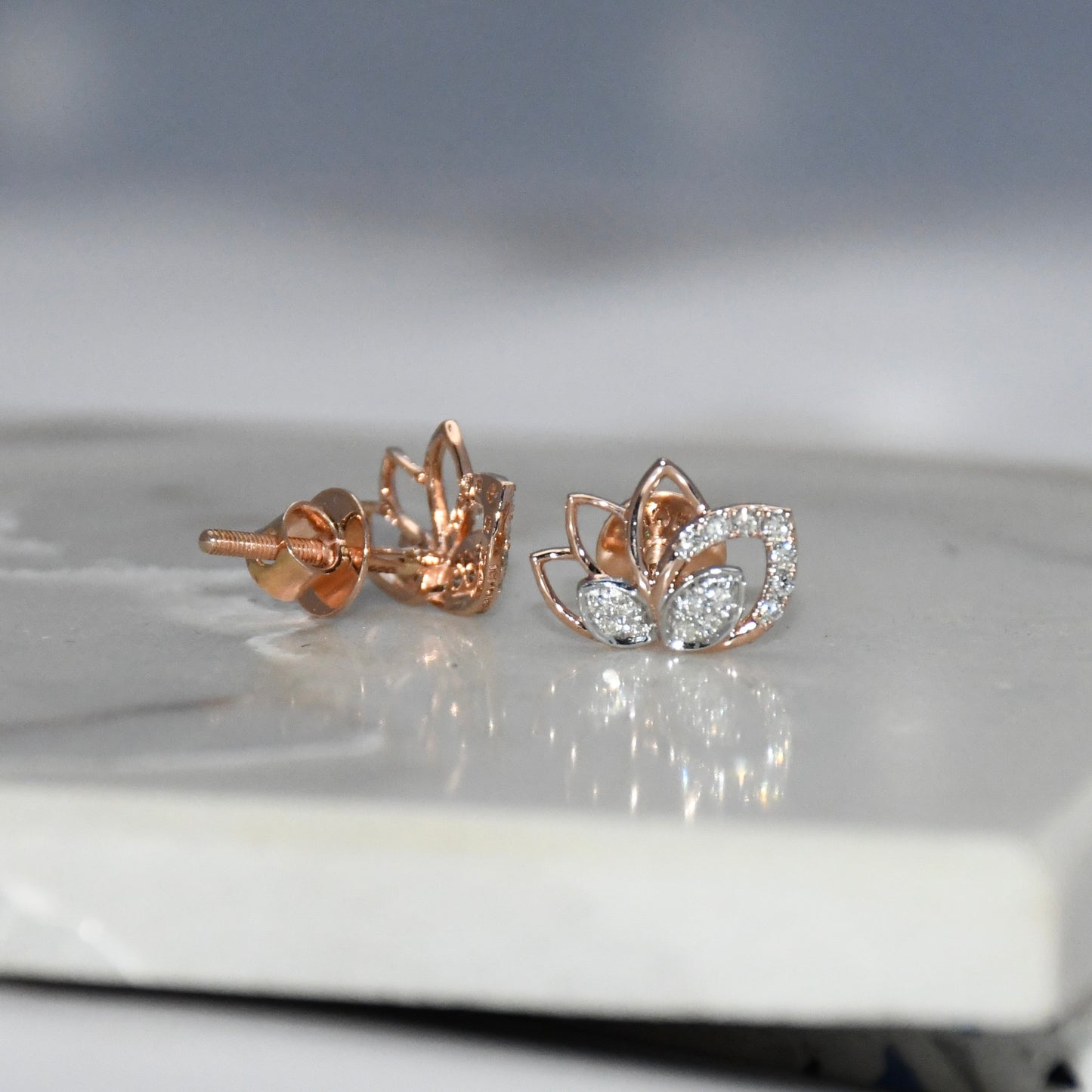Rose gold lotus flower diamond earrings on a reflective surface