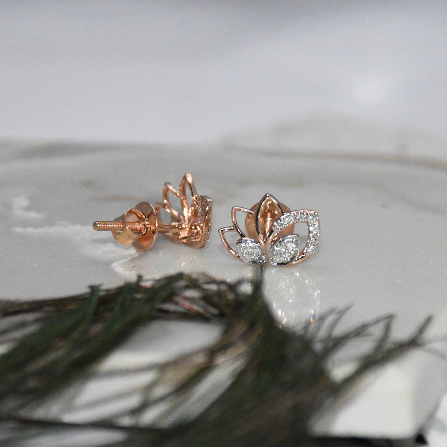 Rose gold lotus flower earrings with clear diamonds on a white surface.