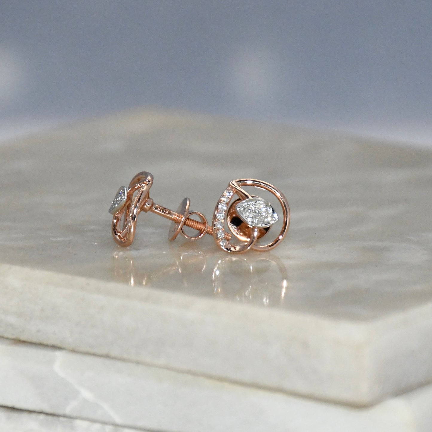 Rose gold earrings with diamond accents on a marble surface