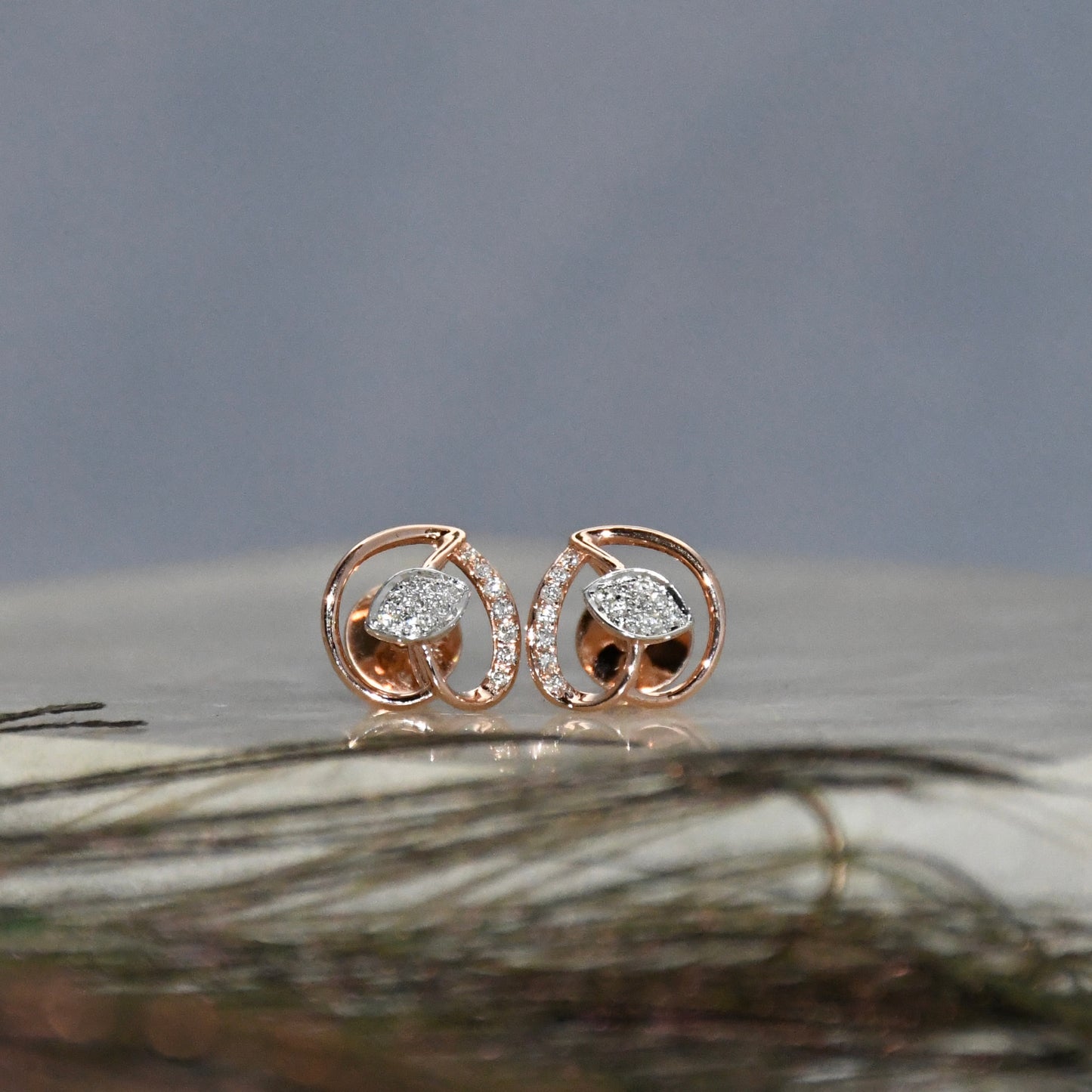 Rose gold earrings with clear diamonds on a textured surface