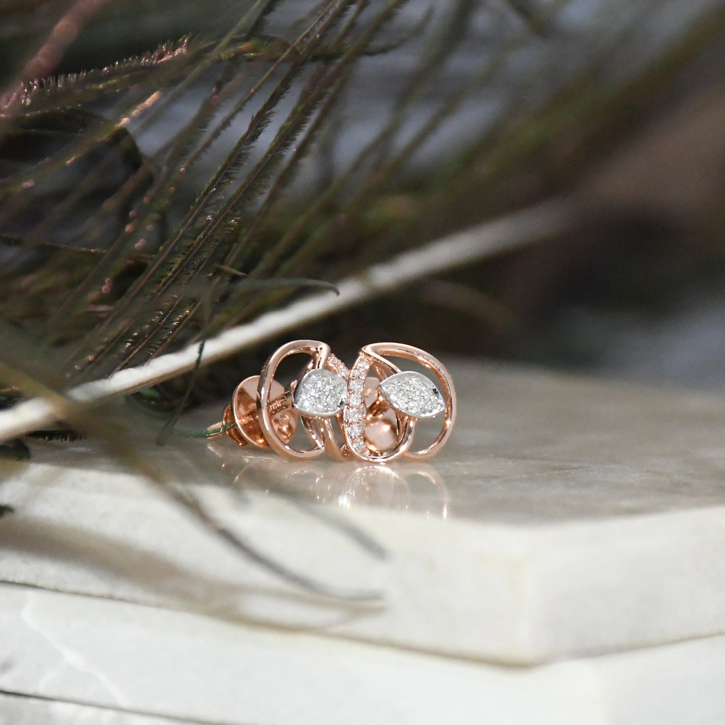 Rose gold earrings with diamonds on a wooden surface with grass in the background