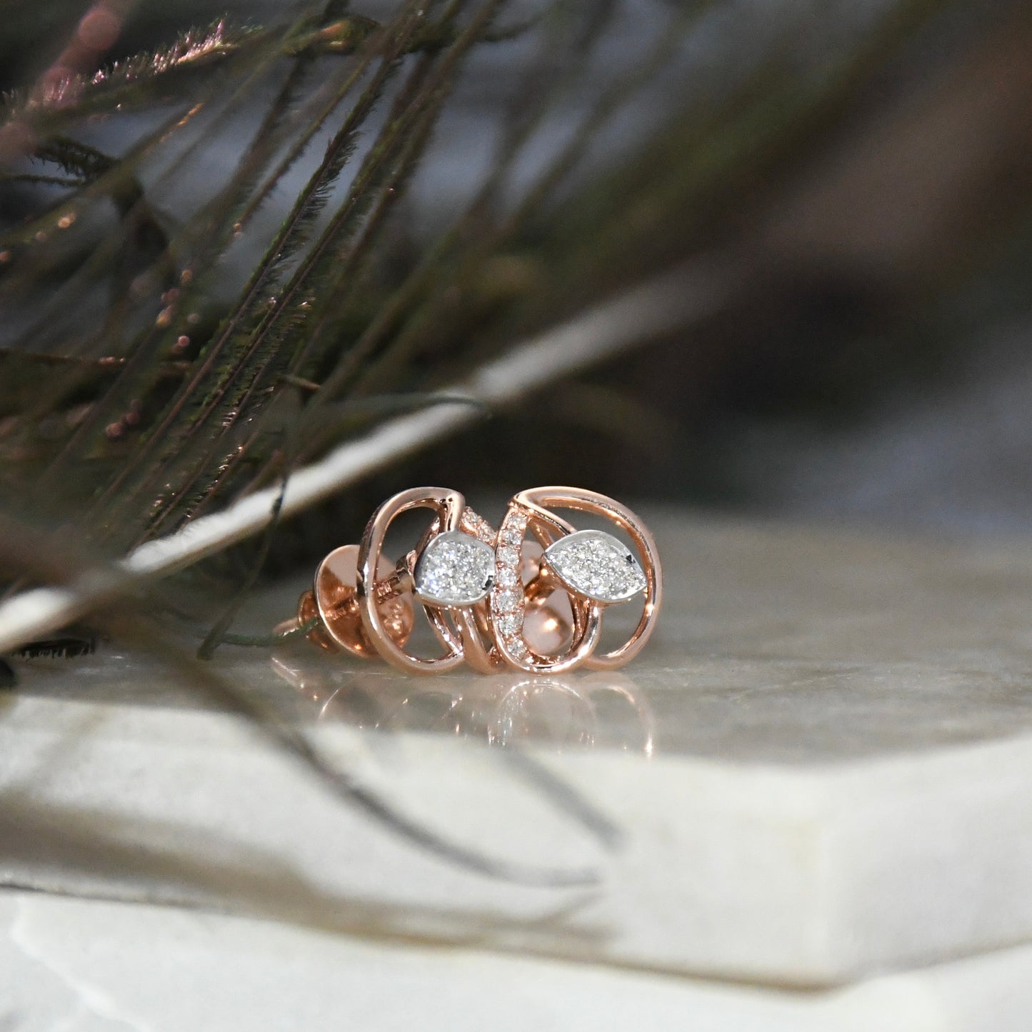 Rose gold earrings with diamonds accents on a textured surface