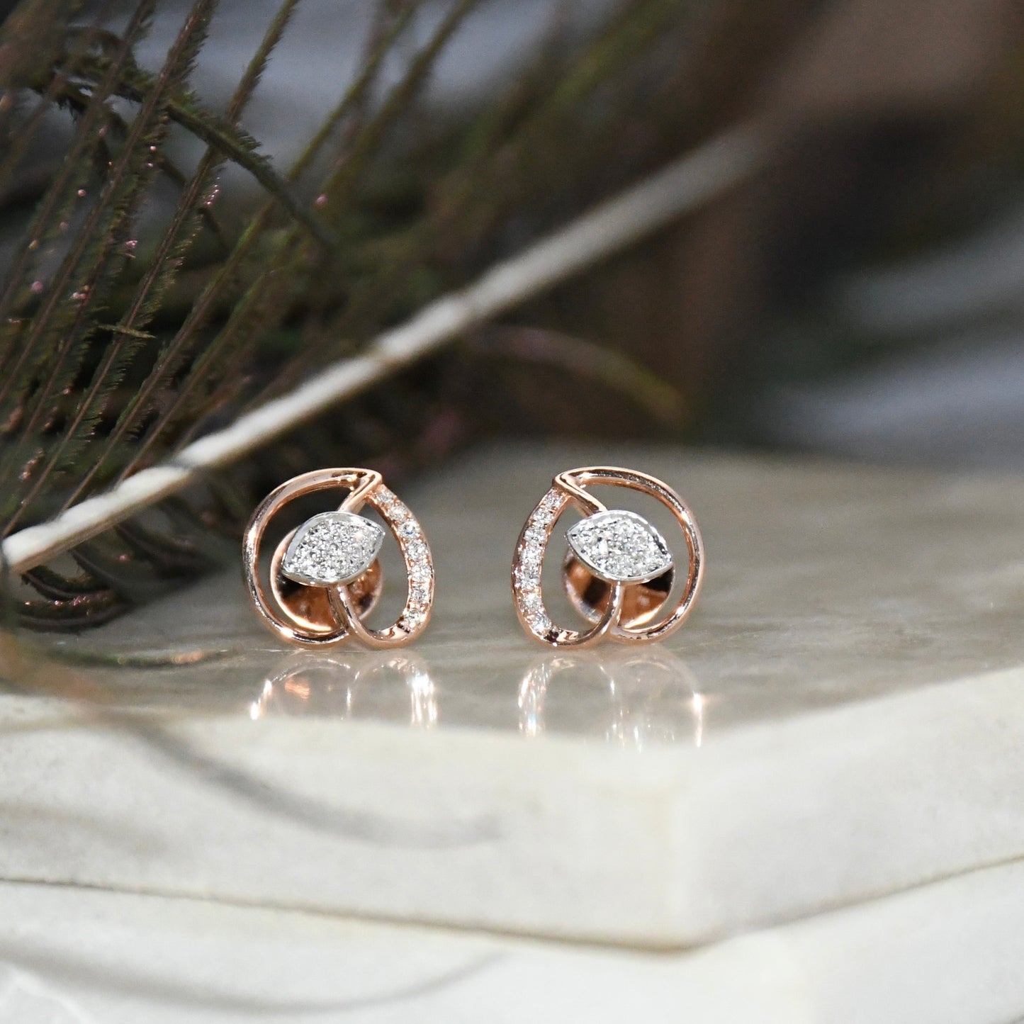 Rose gold earrings with clear diamonds on a marble surface
