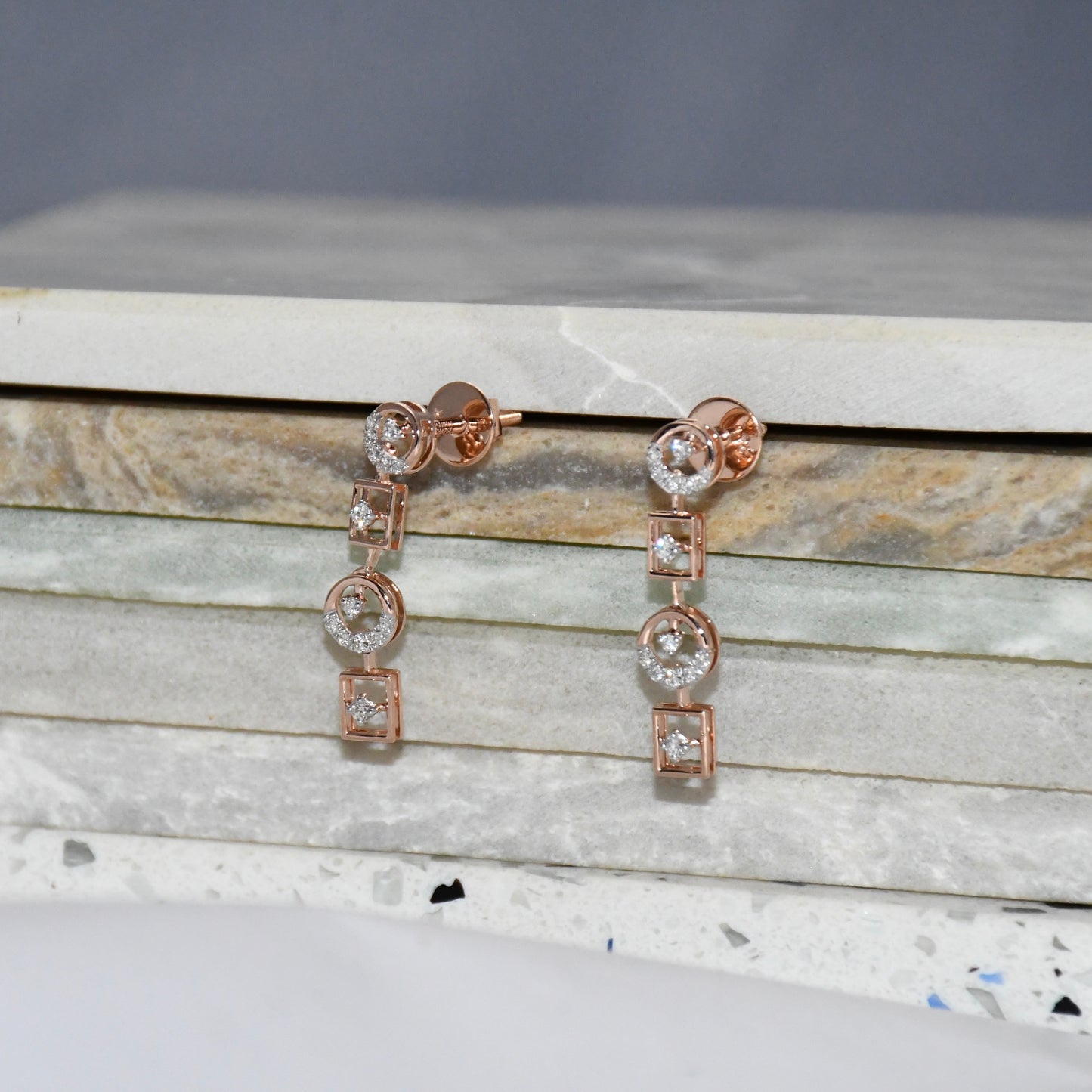 Rose gold earrings with clear diamonds on a marble surface