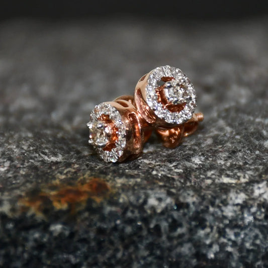 Pair of round halo cluster diamond earrings in gold with center diamonds and surrounding diamond halo, placed on a textured stone surface.