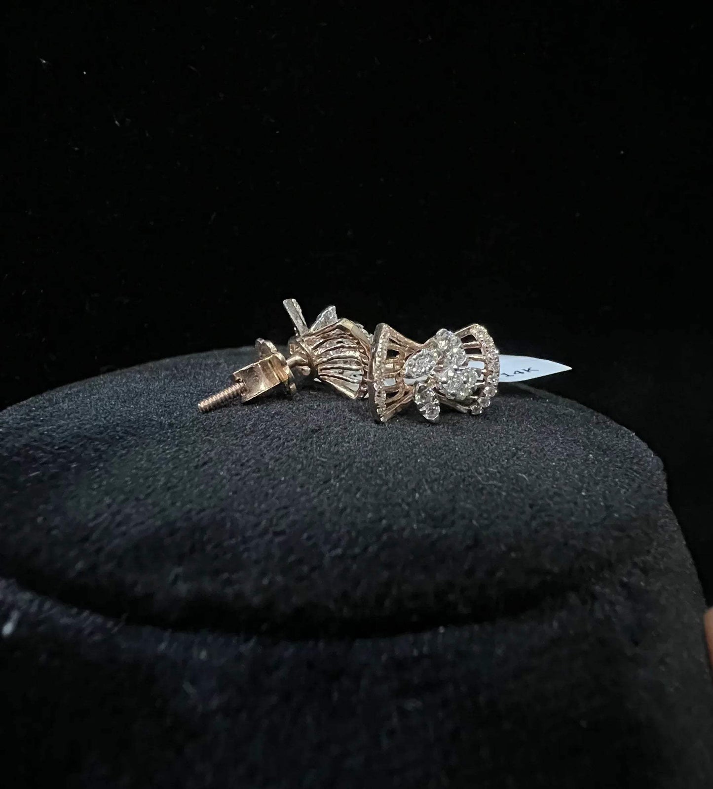 A pair of gold diamond earrings with a round cut design on a mannequin stand.