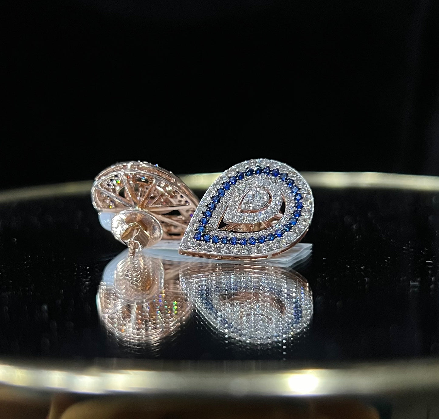 A pair of gold diamond earrings with a geometric pattern, displayed on a reflective surface.