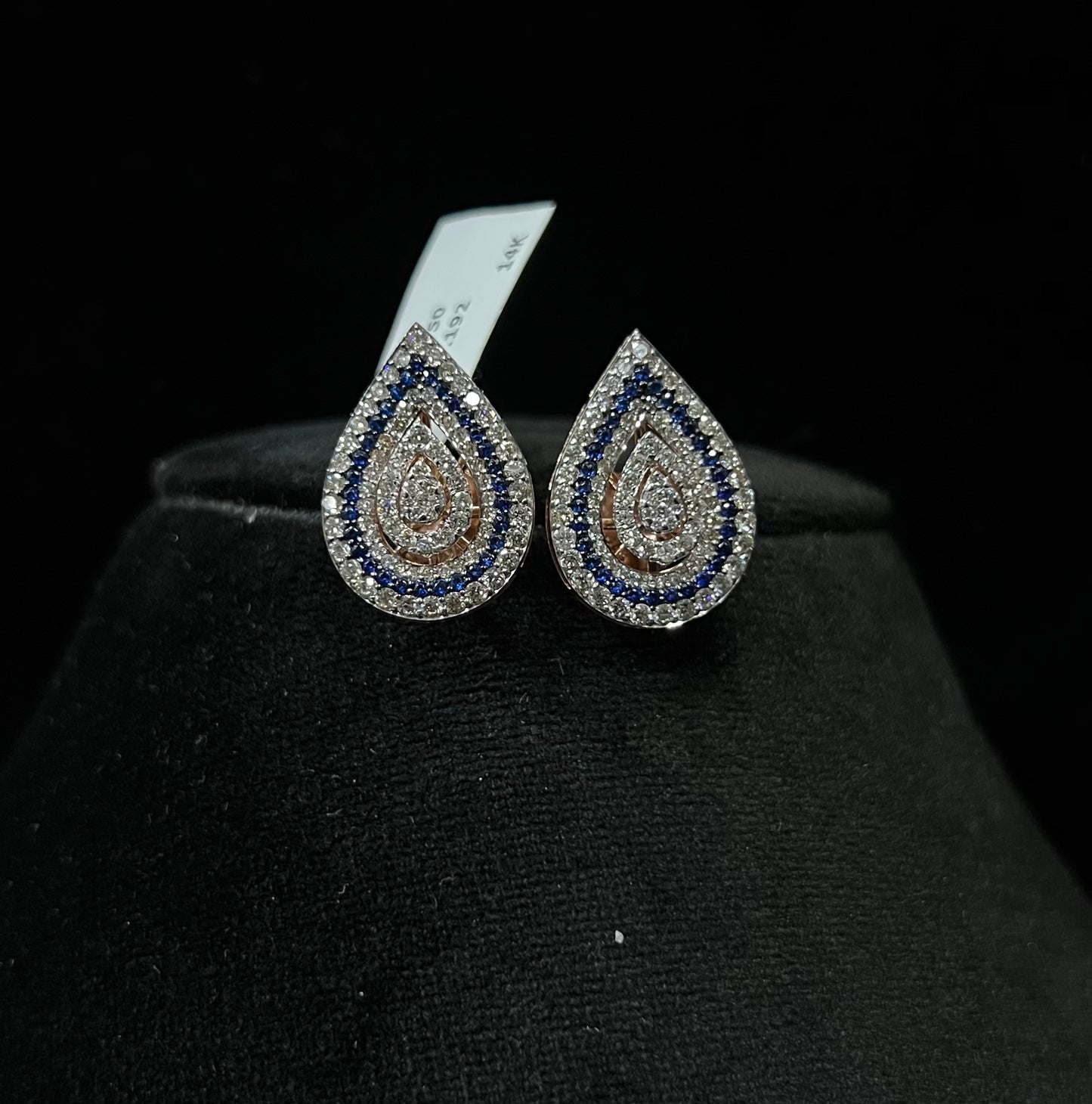 A pair of gold diamond earrings with a geometric pattern, displayed on a mannequin bust.