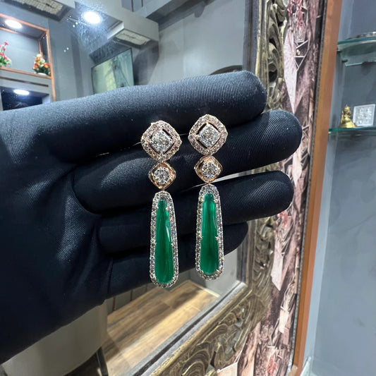 A pair of gold diamond earrings with green color stones set in a minimalist design.