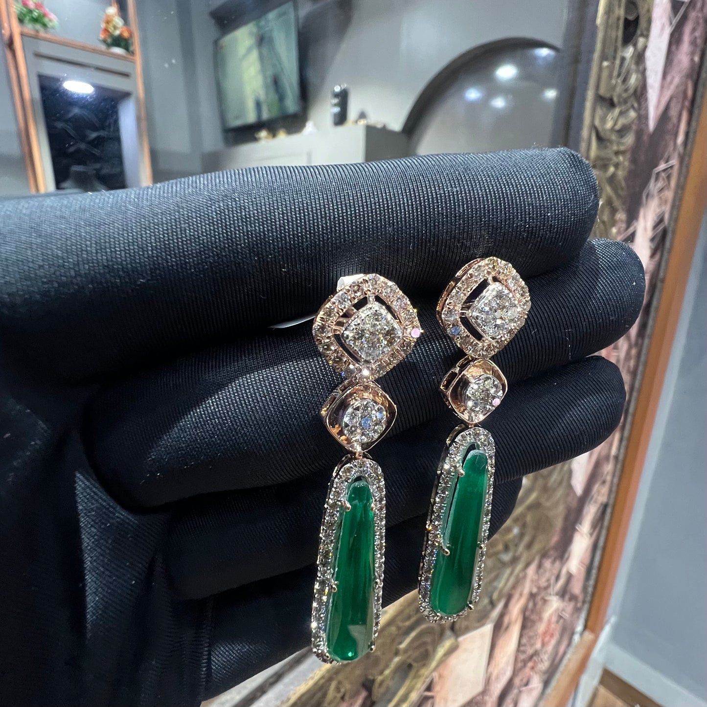 A pair of gold diamond earrings with green color stones set in a minimalist design.