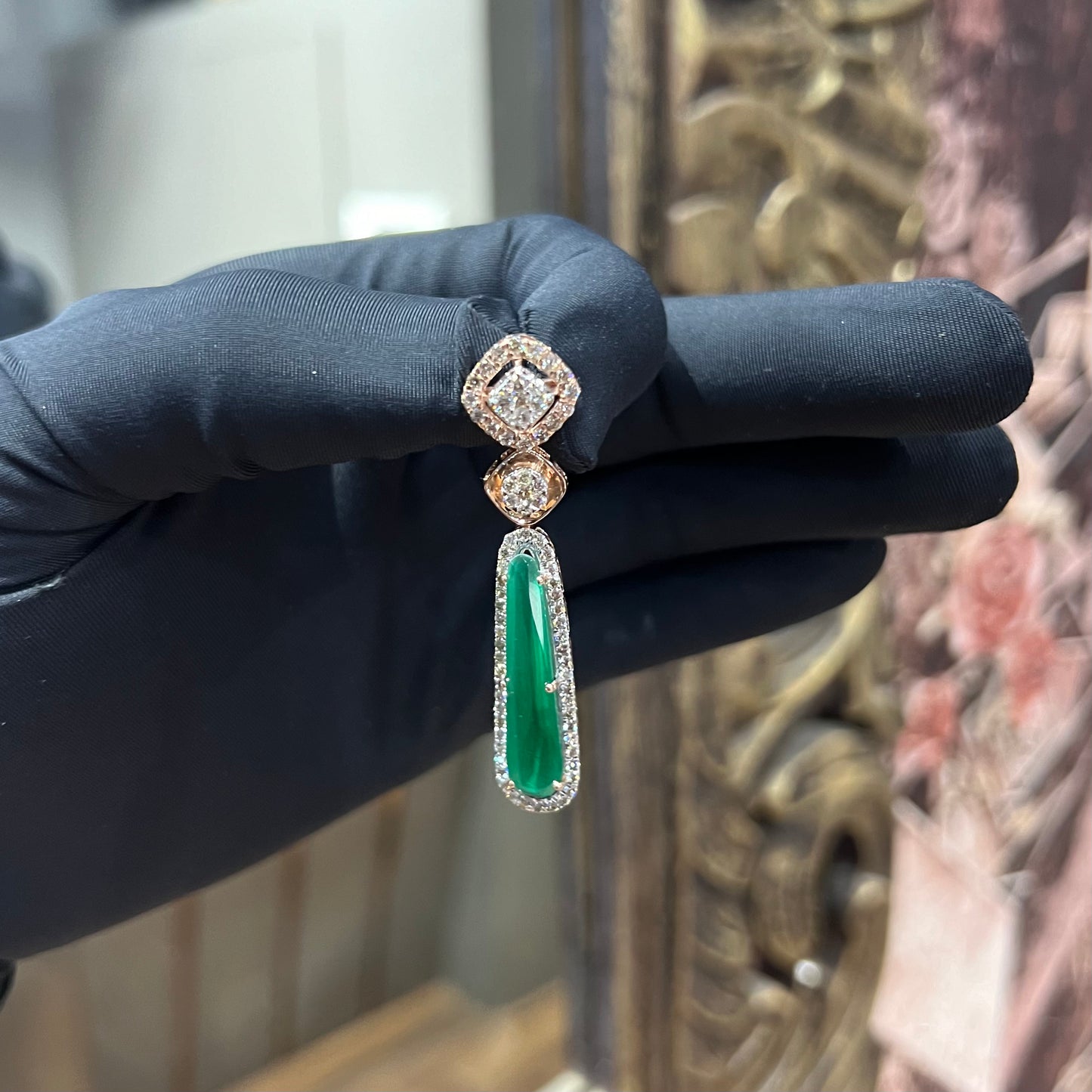 A gold diamond earring with green color stones set in a minimalist design.