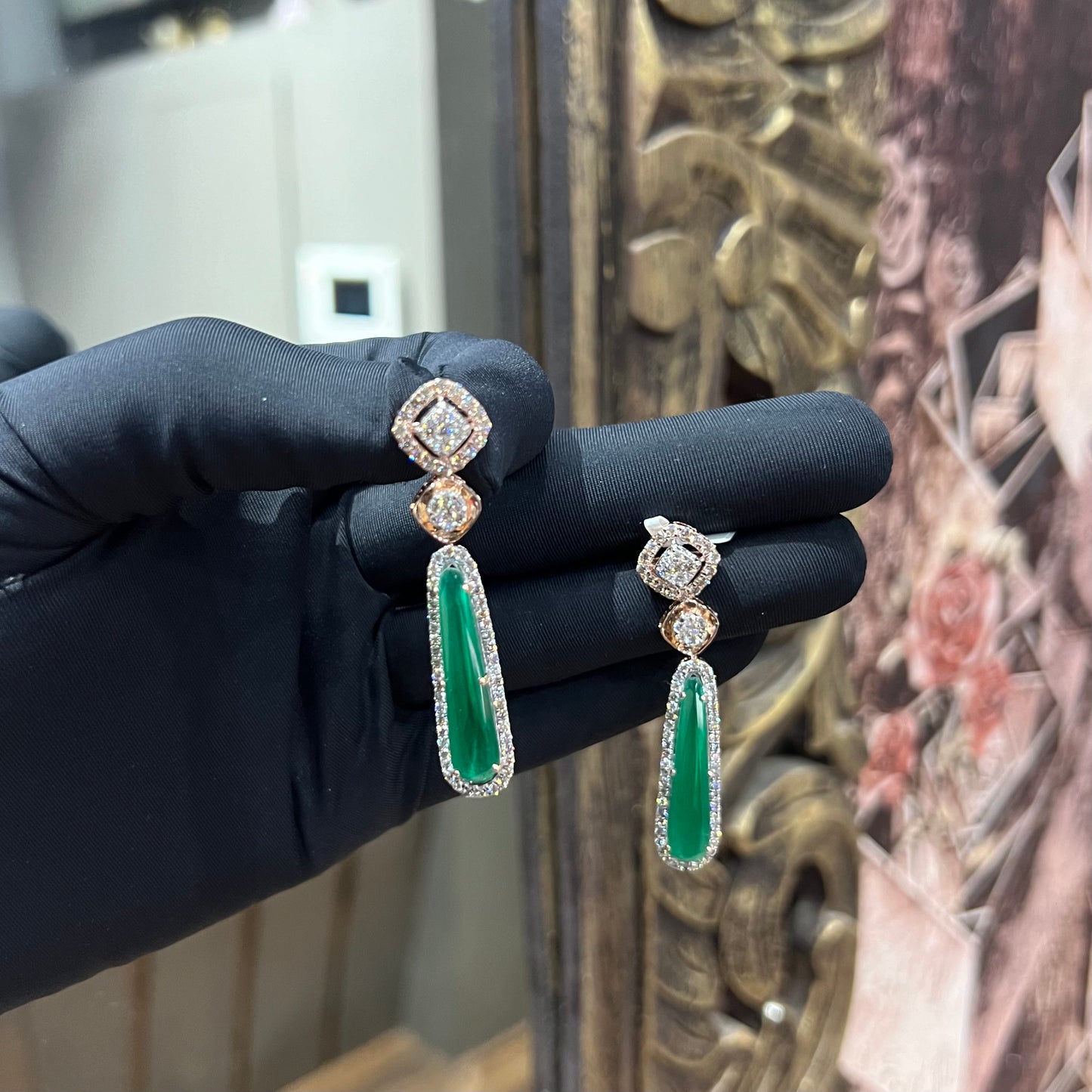 A pair of gold diamond earrings with green color stones set in a minimalist design.
